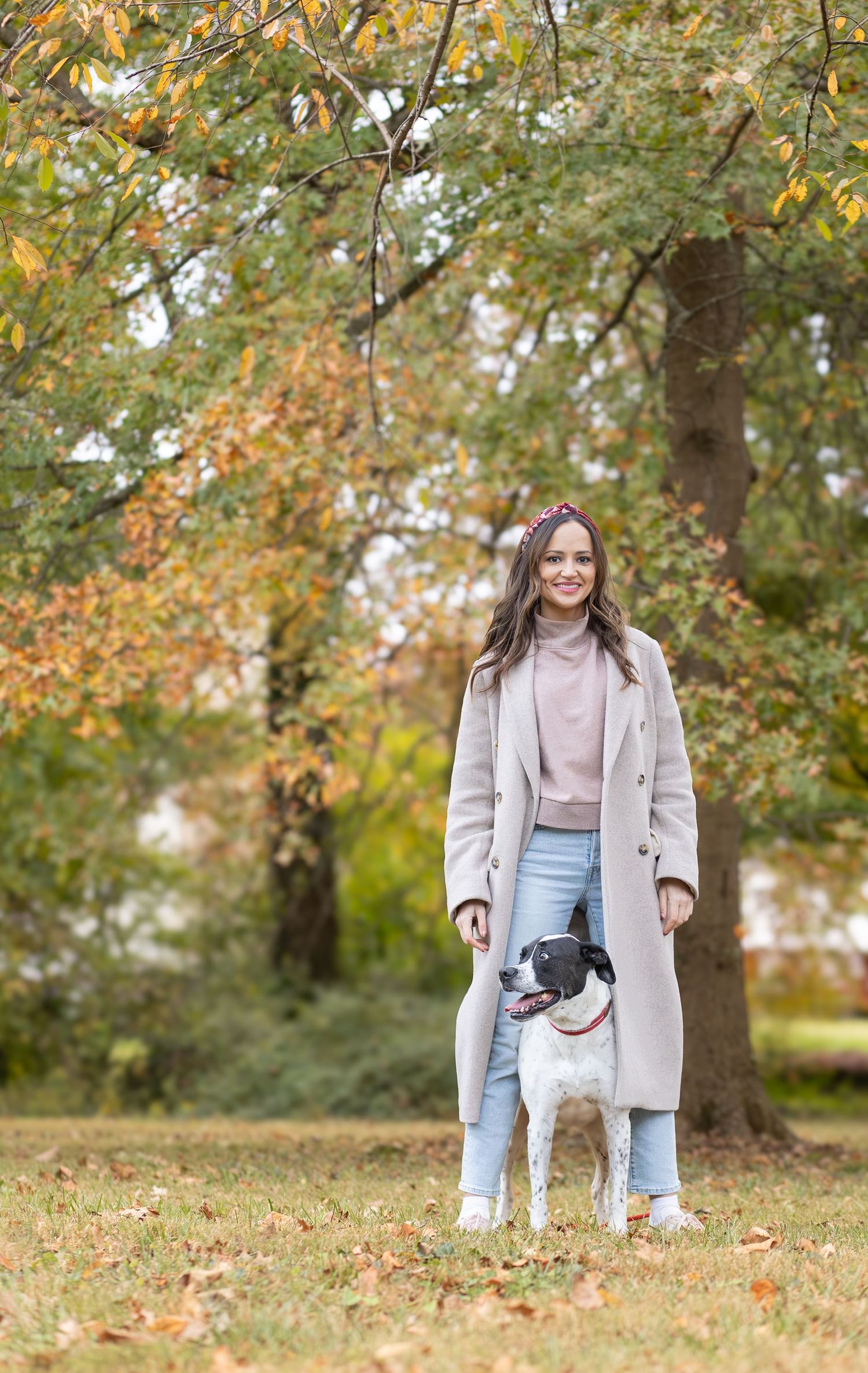 Woman standing with her dog under fall trees