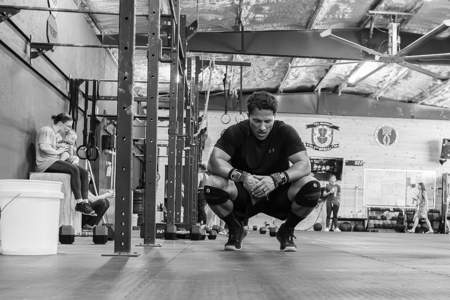 Black and white photo of a man squatting in a CrossFit gym