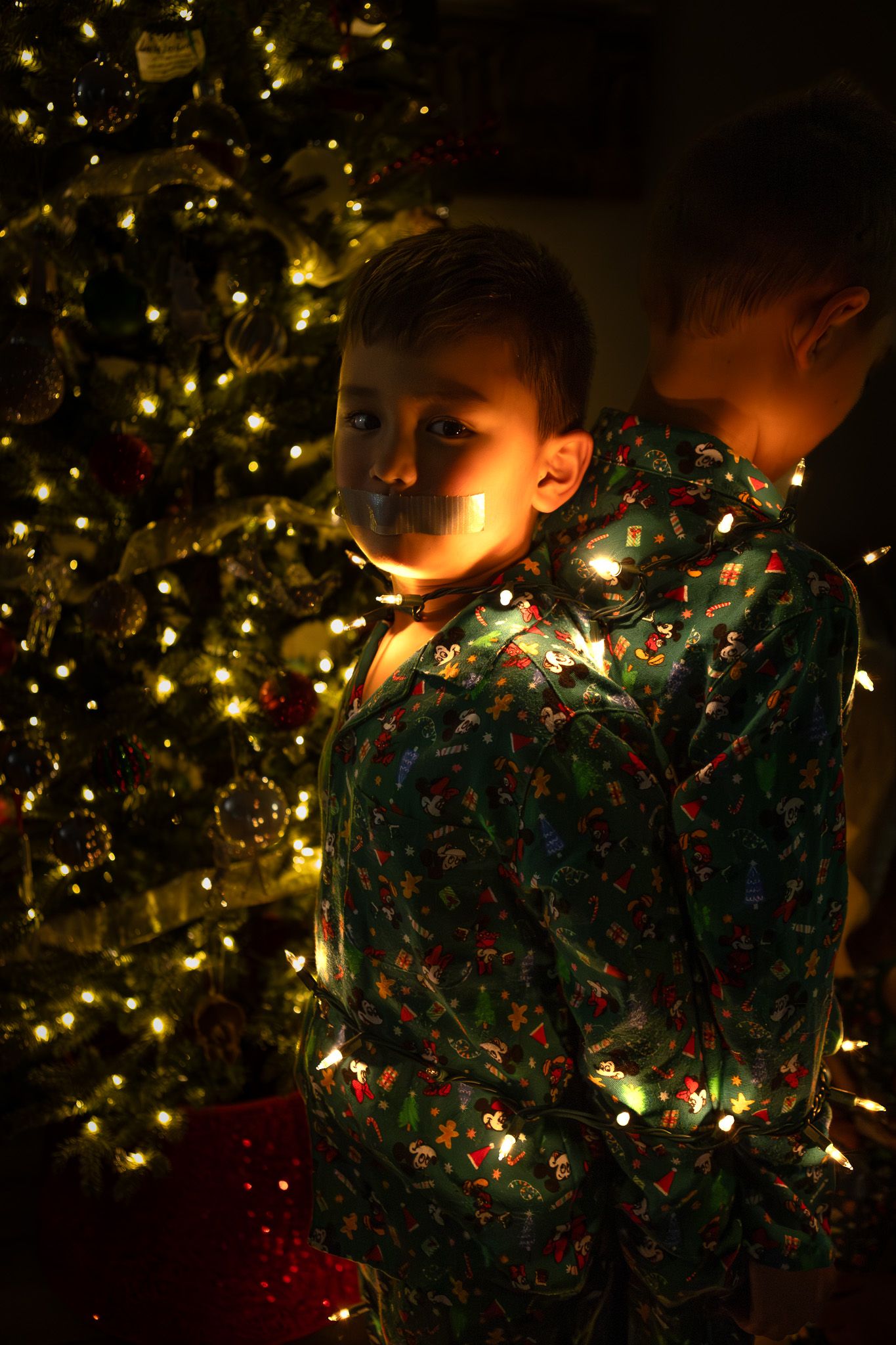 Boy in Christmas pajamas lit by twinkle lights by the tree