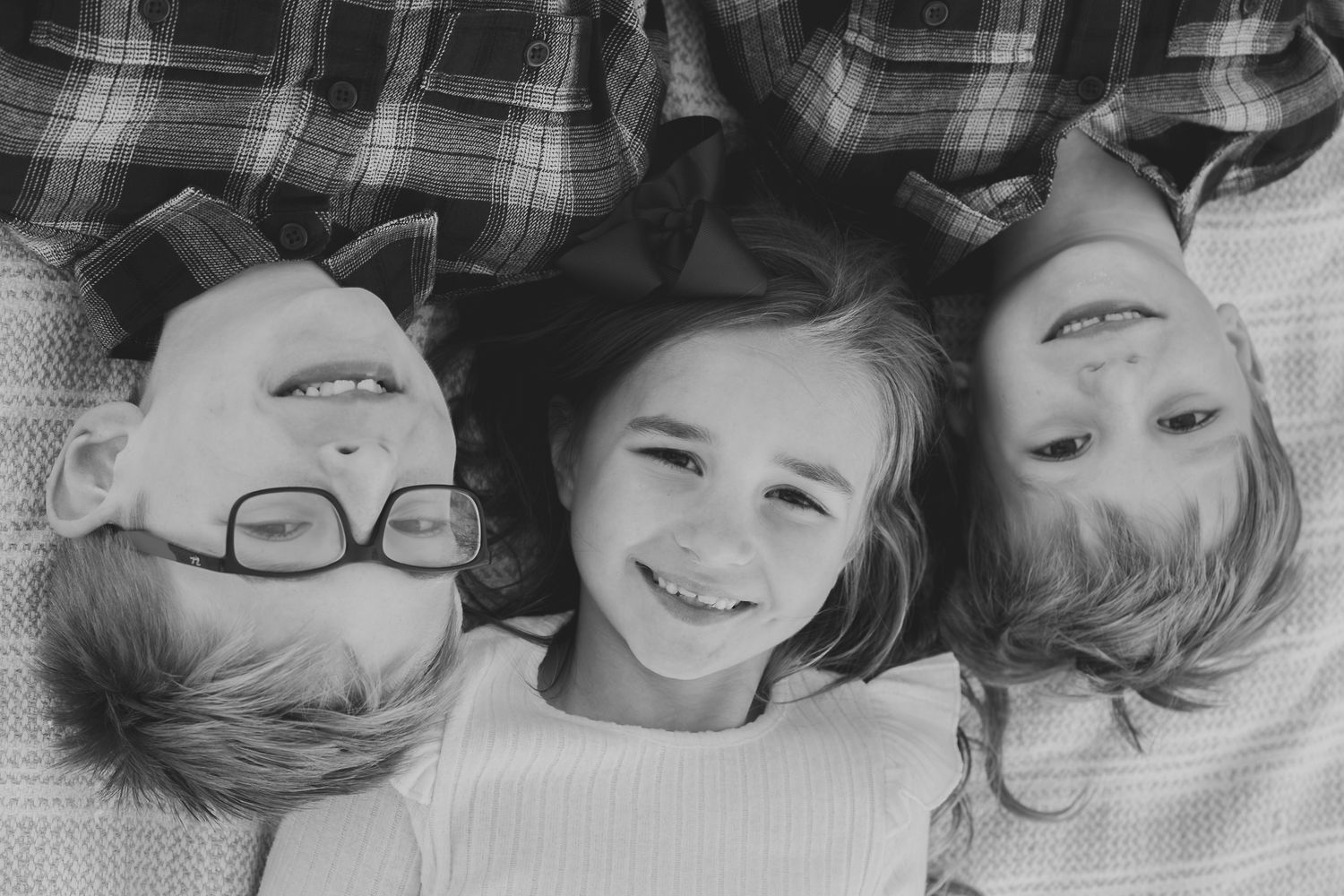 Black and white photo of three siblings lying head to head, smiling up at the camera