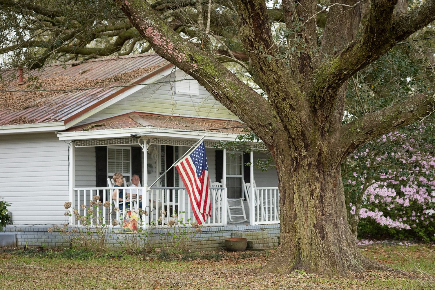 White farmhouse with an American flag under a large oak tree