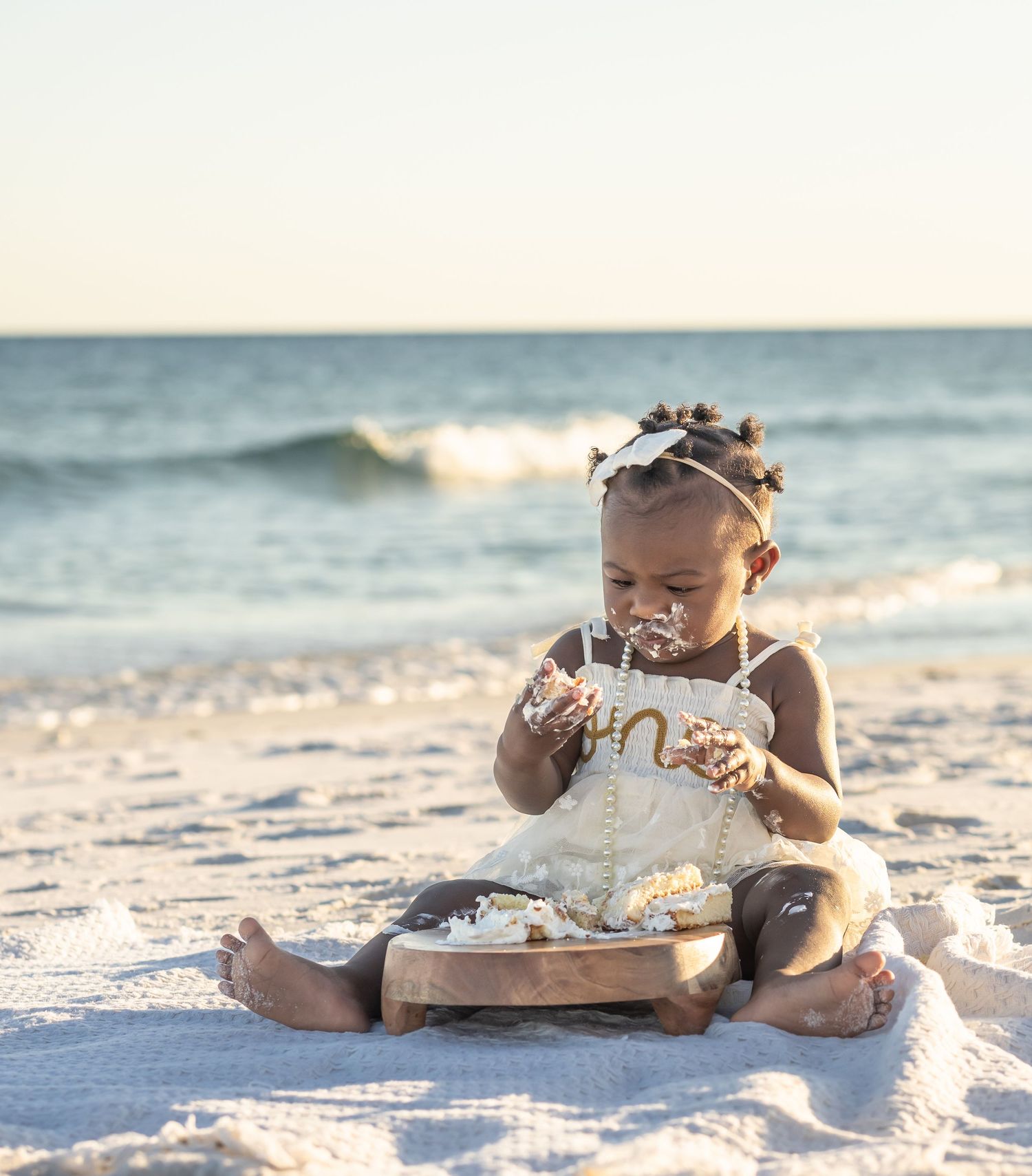 Baby girl sitting on the beach by the waves for her first birthday
