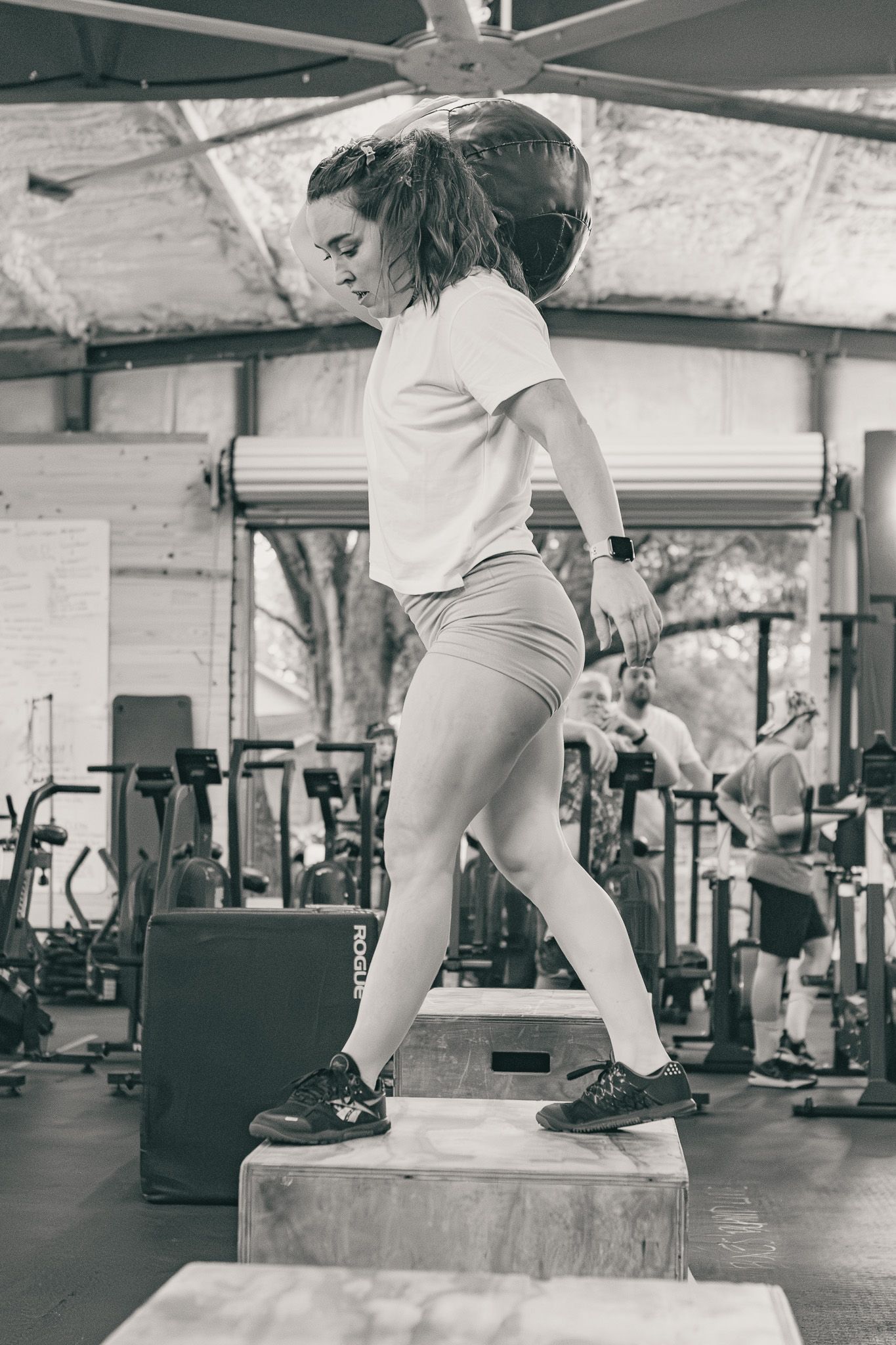 Black and white photo of a woman doing box step-ups at the gym