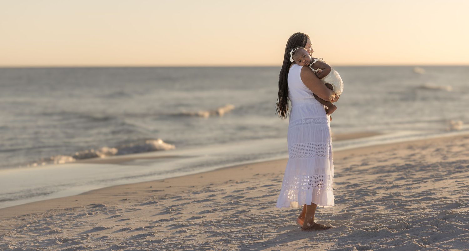 Woman in a white dress walking along the shoreline at sunset
