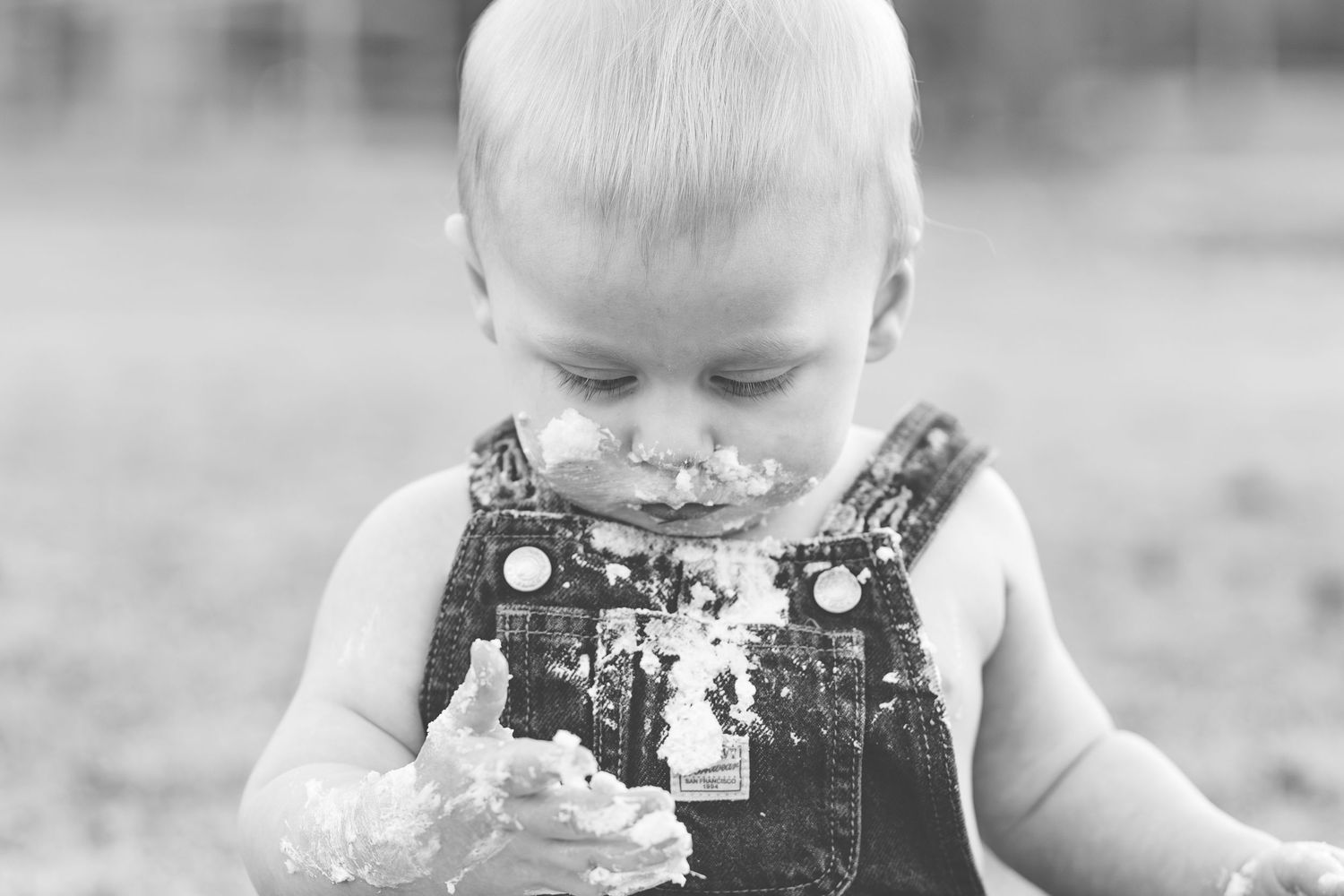 Black and white photo of a baby boy in overalls at his cake smash