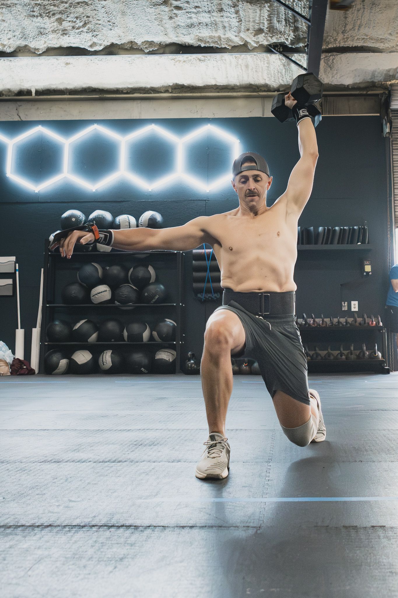 Man doing an overhead dumbbell lunge at a CrossFit gym