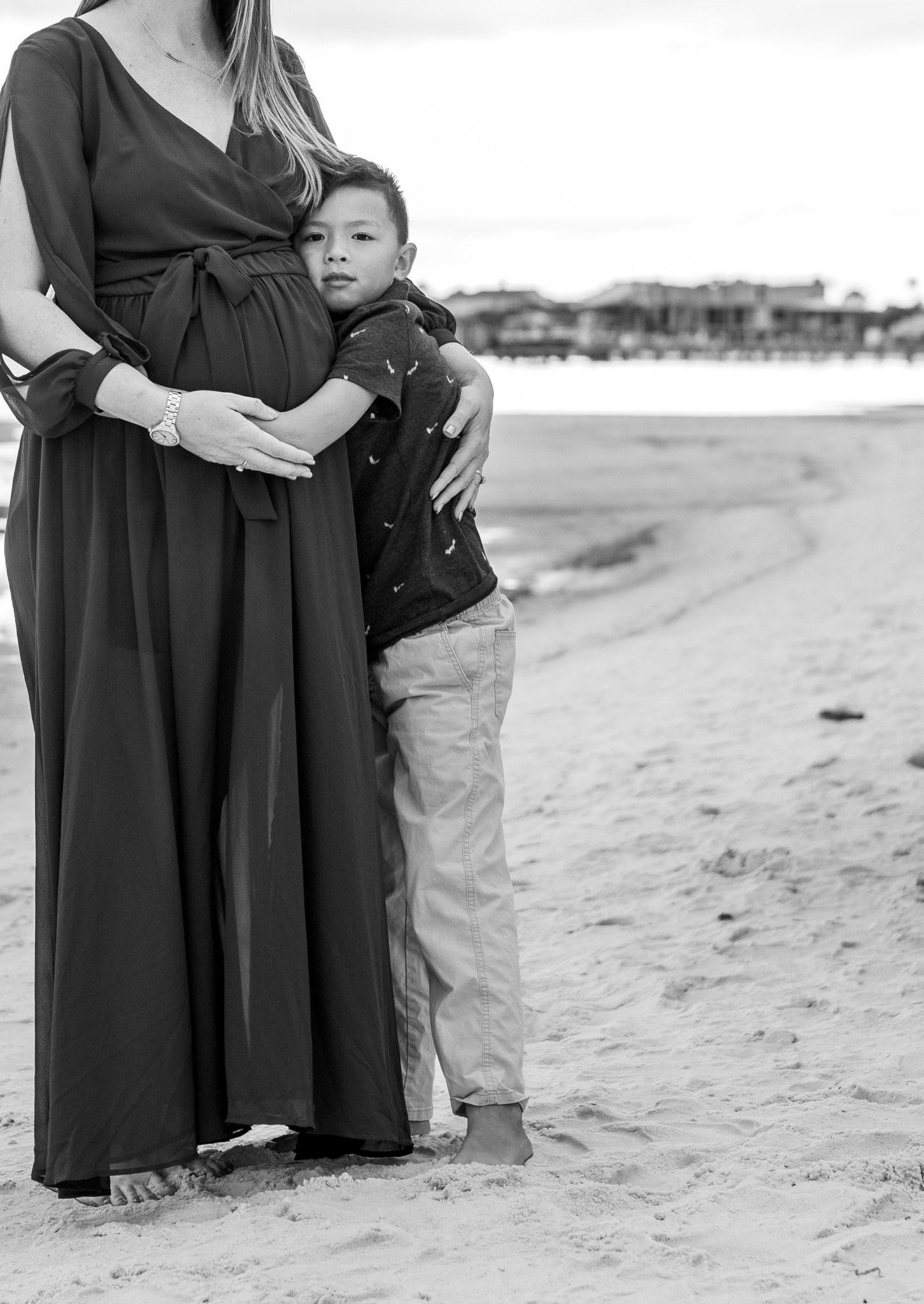 Black and white photo of a pregnant mom hugging her son on the beach