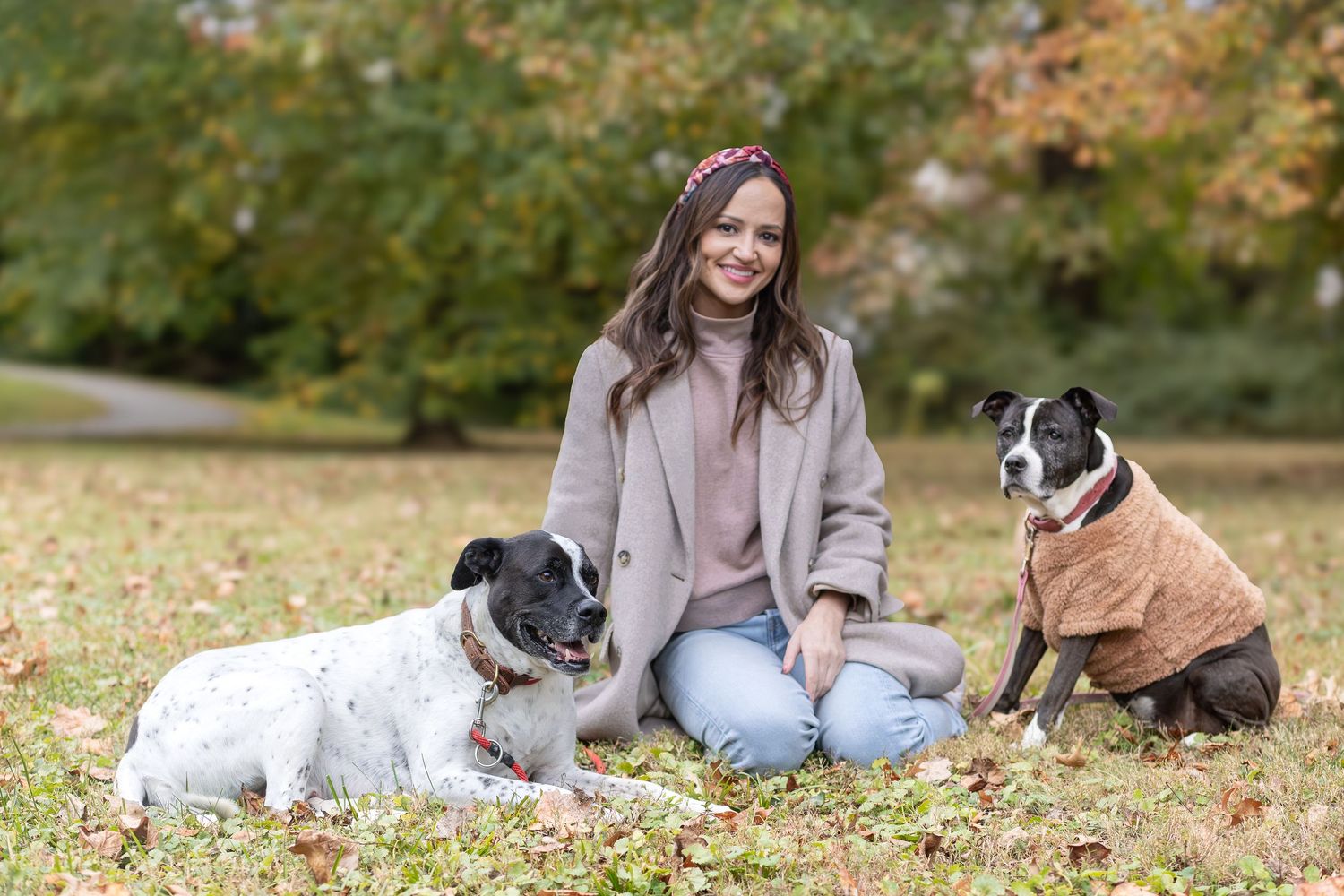 Woman sitting in the grass with her two dogs in sweaters for fall photos