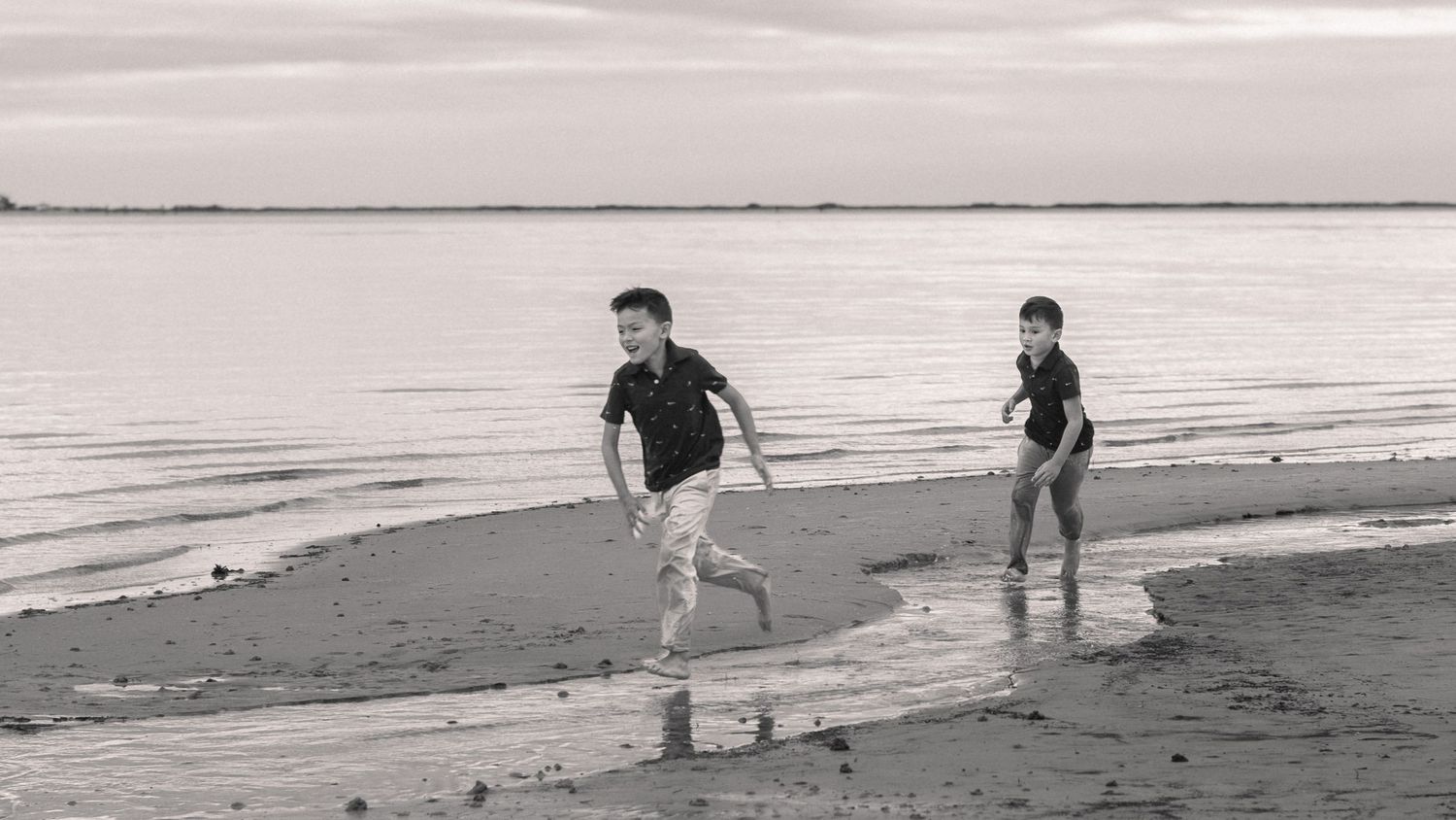 Two boys running along the water's edge at sunset