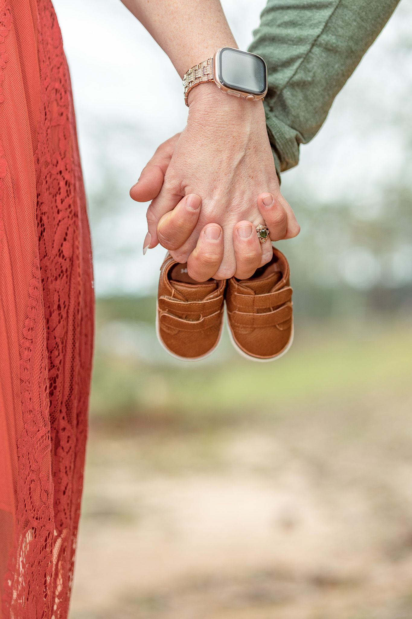 Parents-to-be holding hands and a tiny pair of baby shoes