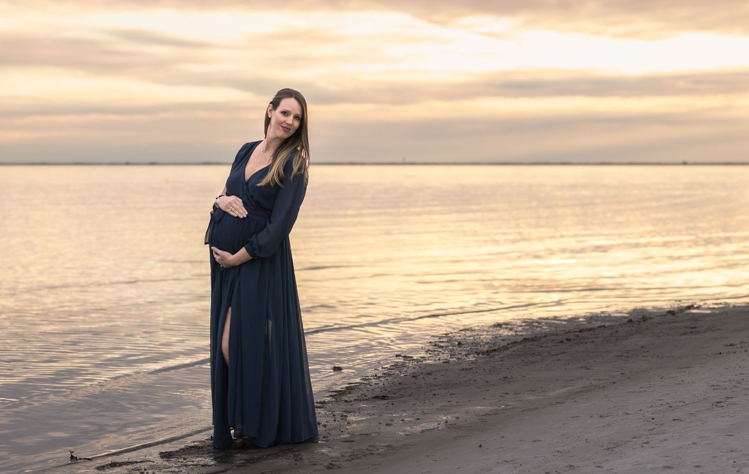 Maternity portrait of a mom standing at the water's edge at sunset
