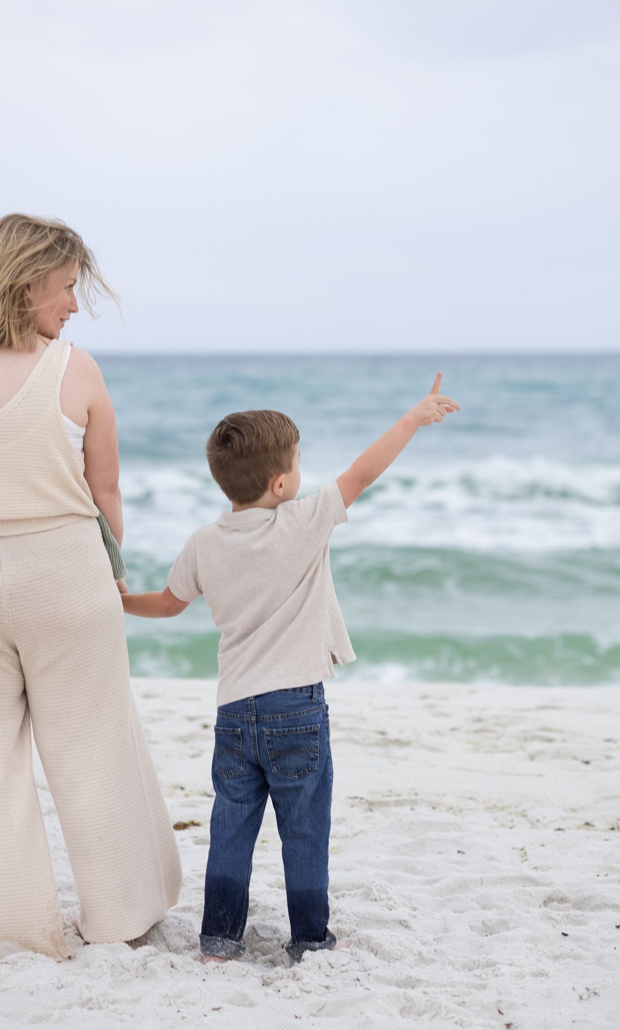 Little boy pointing at the ocean while standing with his mom