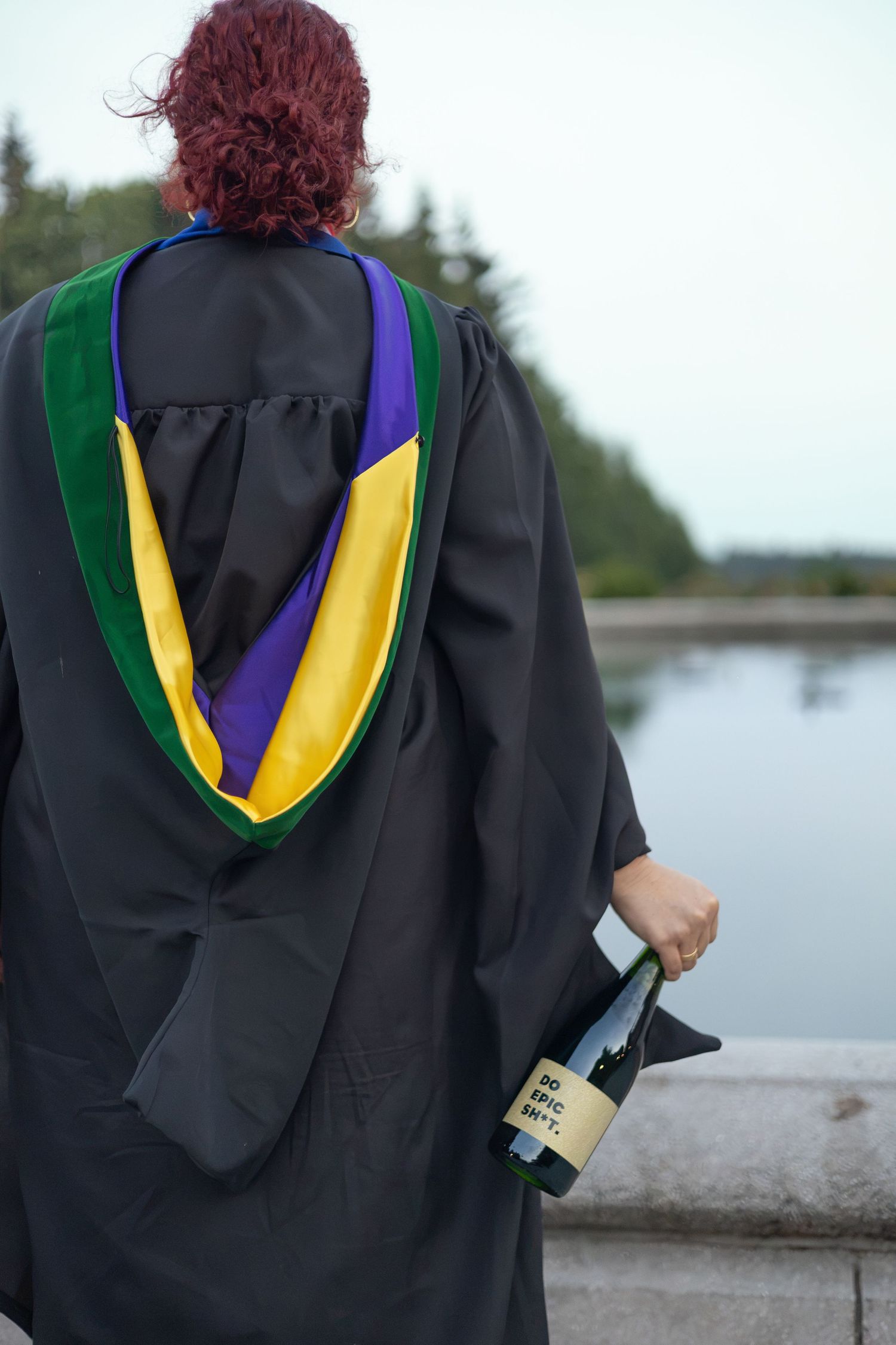Graduate in her gown and colorful hood holding a bottle of champagne