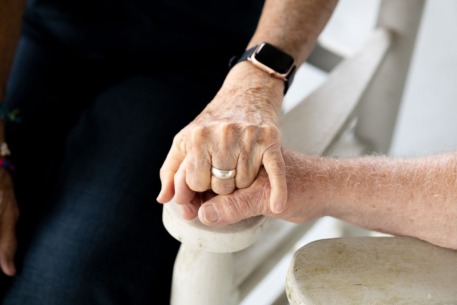 Close-up of an older couple holding hands on a porch rocking chair