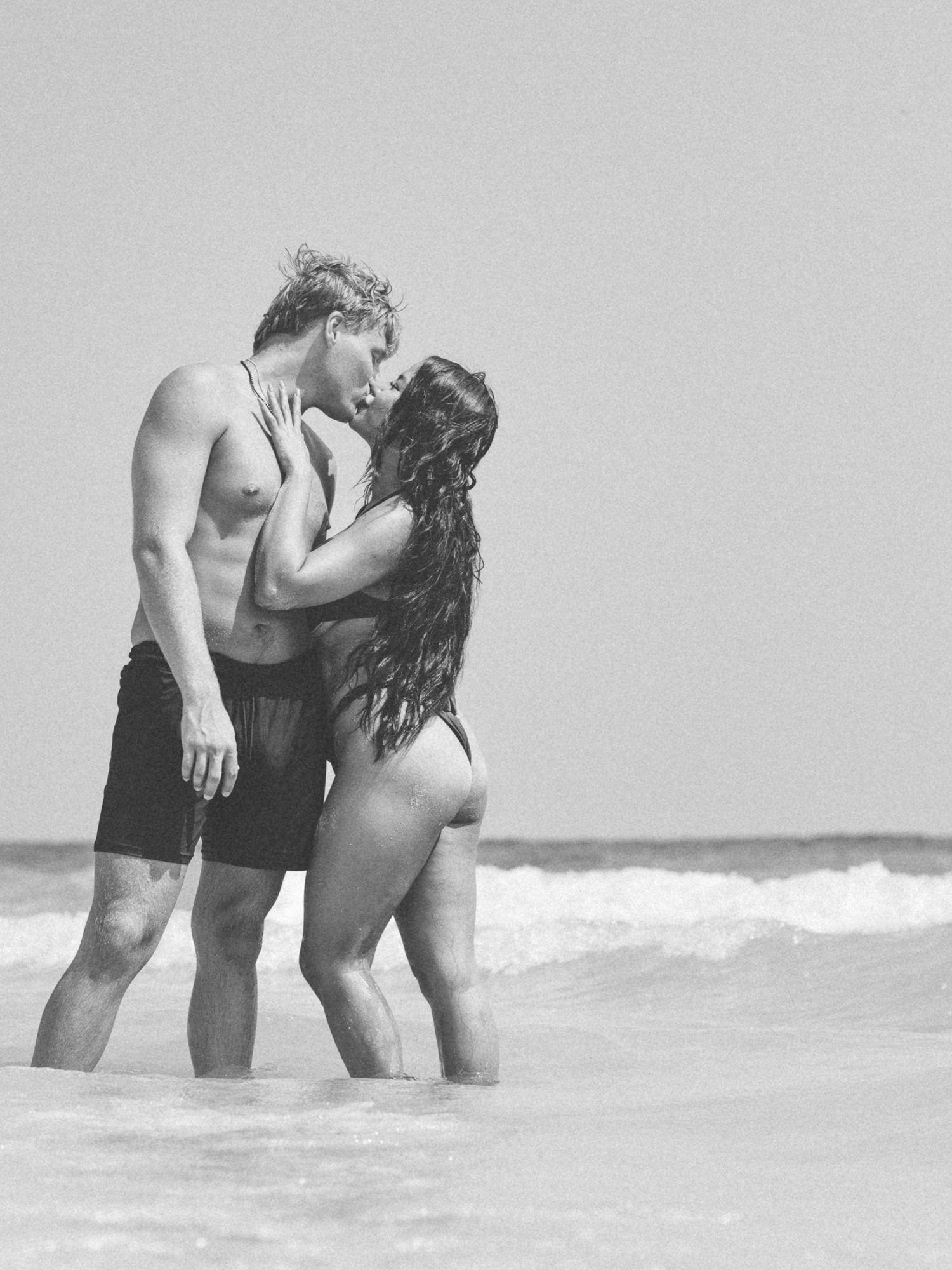 Black and white photo of a couple kissing in the Gulf surf