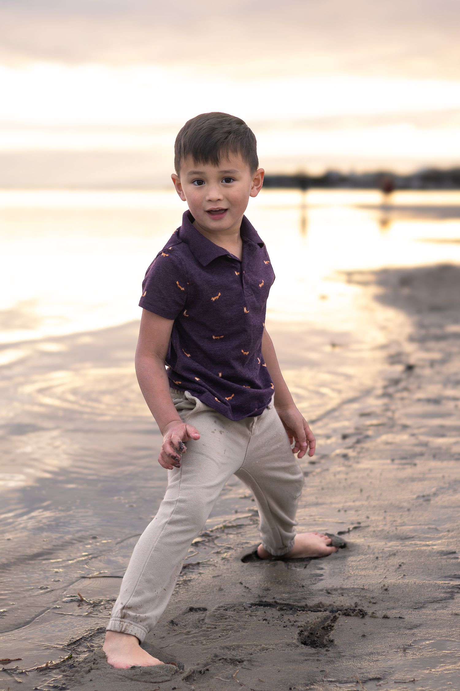 Barefoot boy posing playfully on the beach at sunset