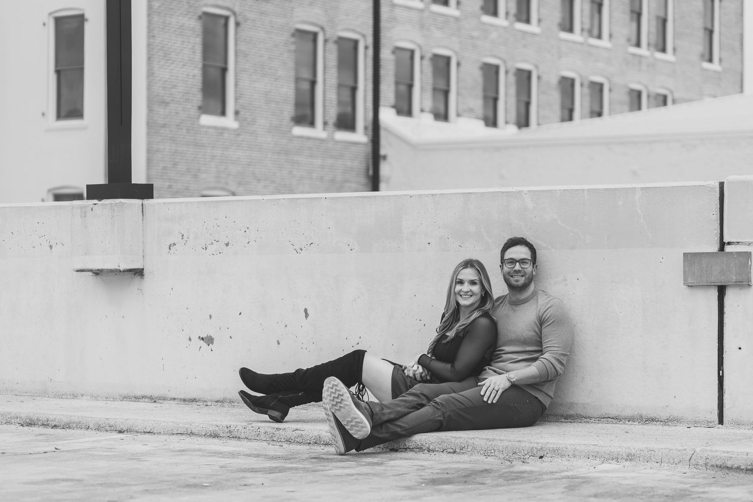 Black and white photo of a couple sitting against a downtown building