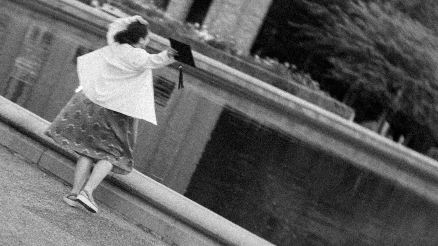 Black and white photo of a graduate sitting on a ledge