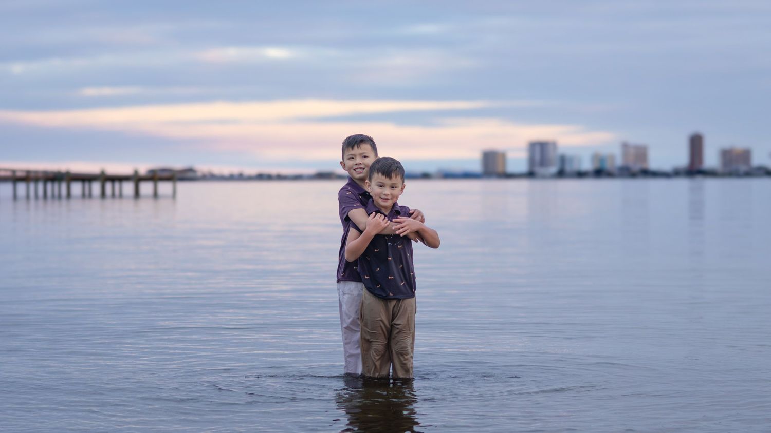 Kids standing in the bay at sunset with the city skyline behind them