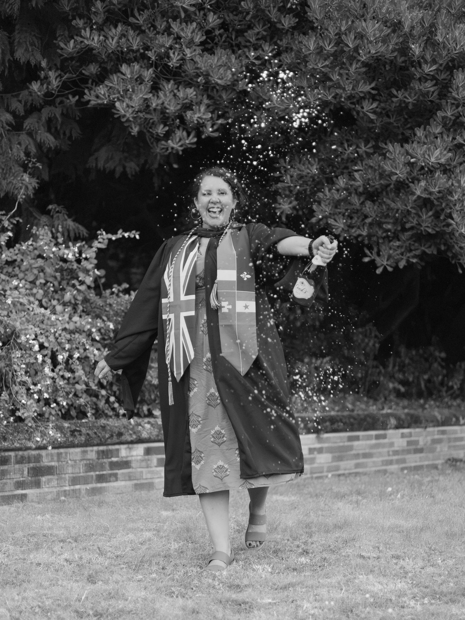 Black and white photo of a graduate celebrating outdoors in her gown