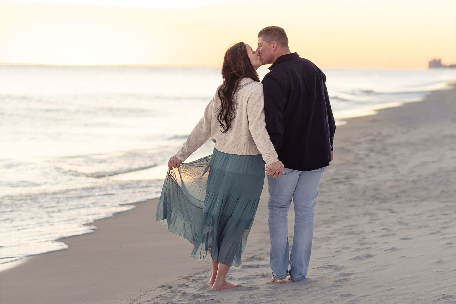 Couple kissing while walking along the beach at sunset