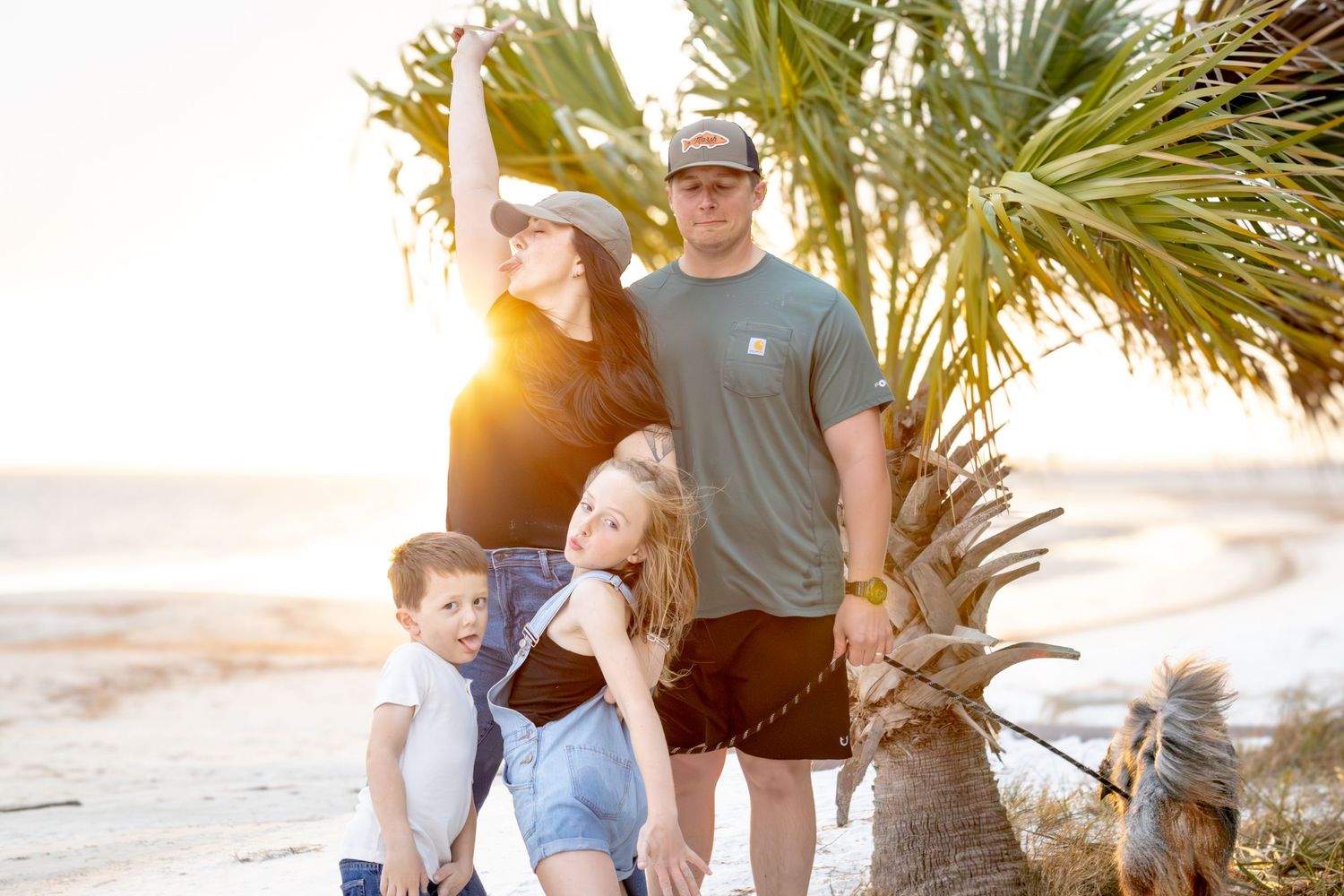 Family laughing together under palm trees on the beach at sunset