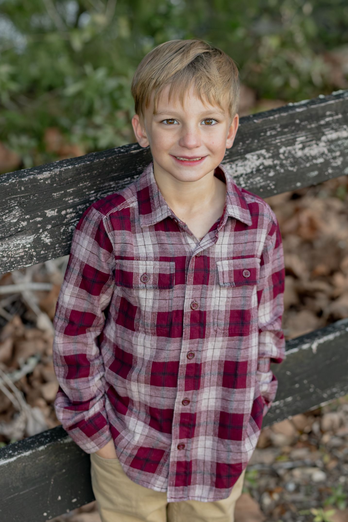 Smiling boy in a red plaid shirt leaning on a wooden fence