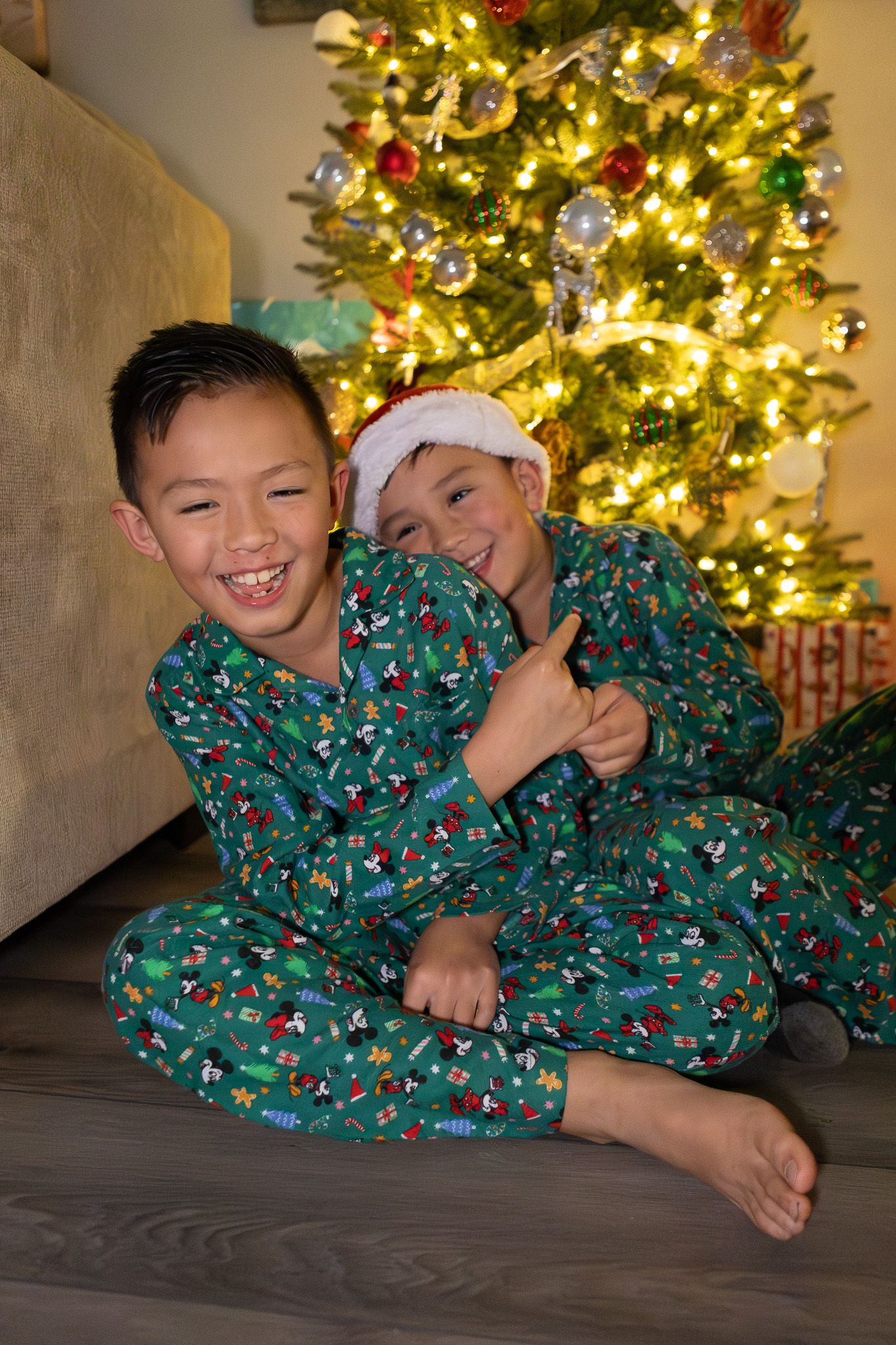 Two brothers in matching Christmas pajamas laughing by the tree