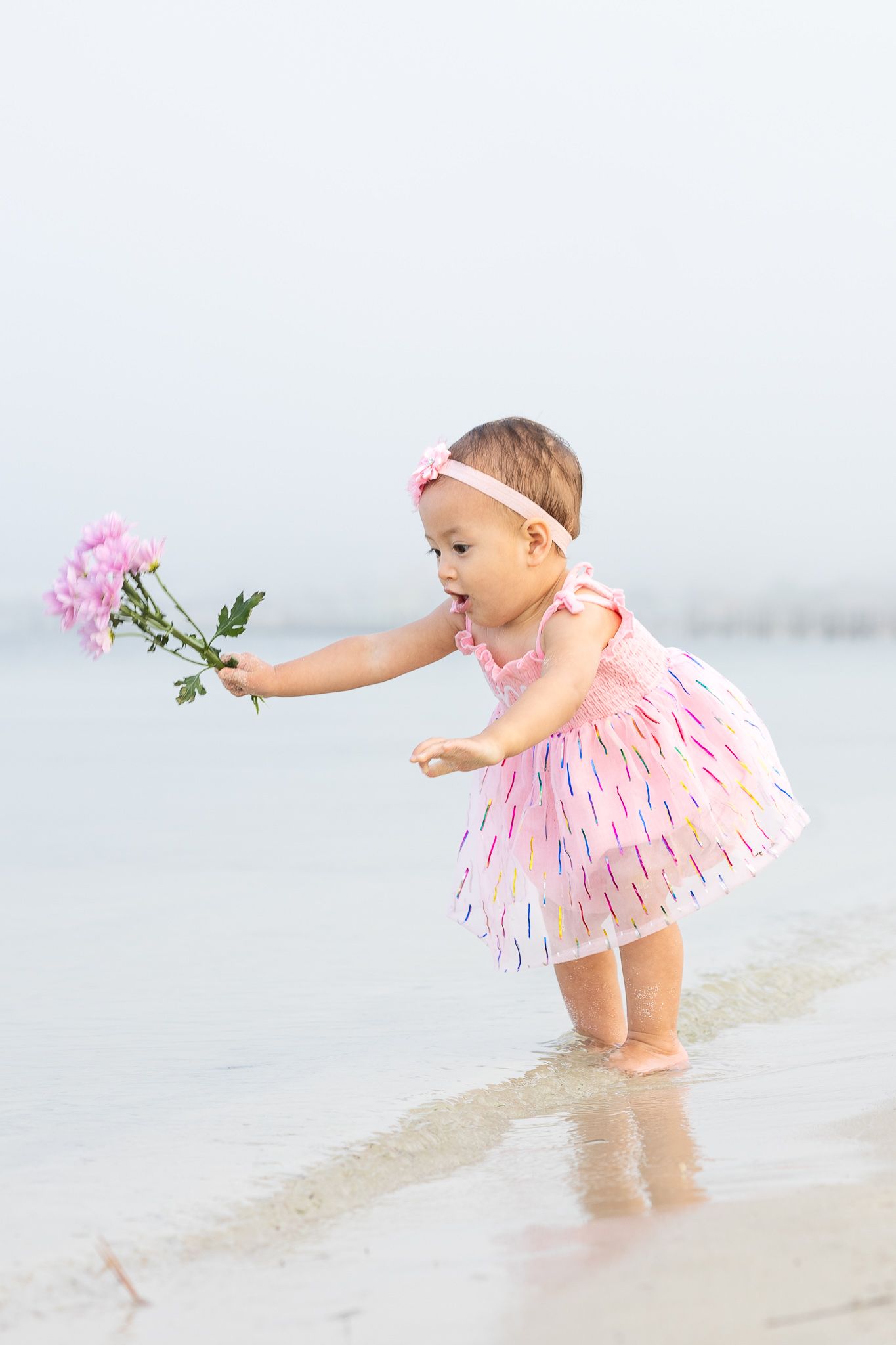 Baby girl holding a pink flower at the edge of the water