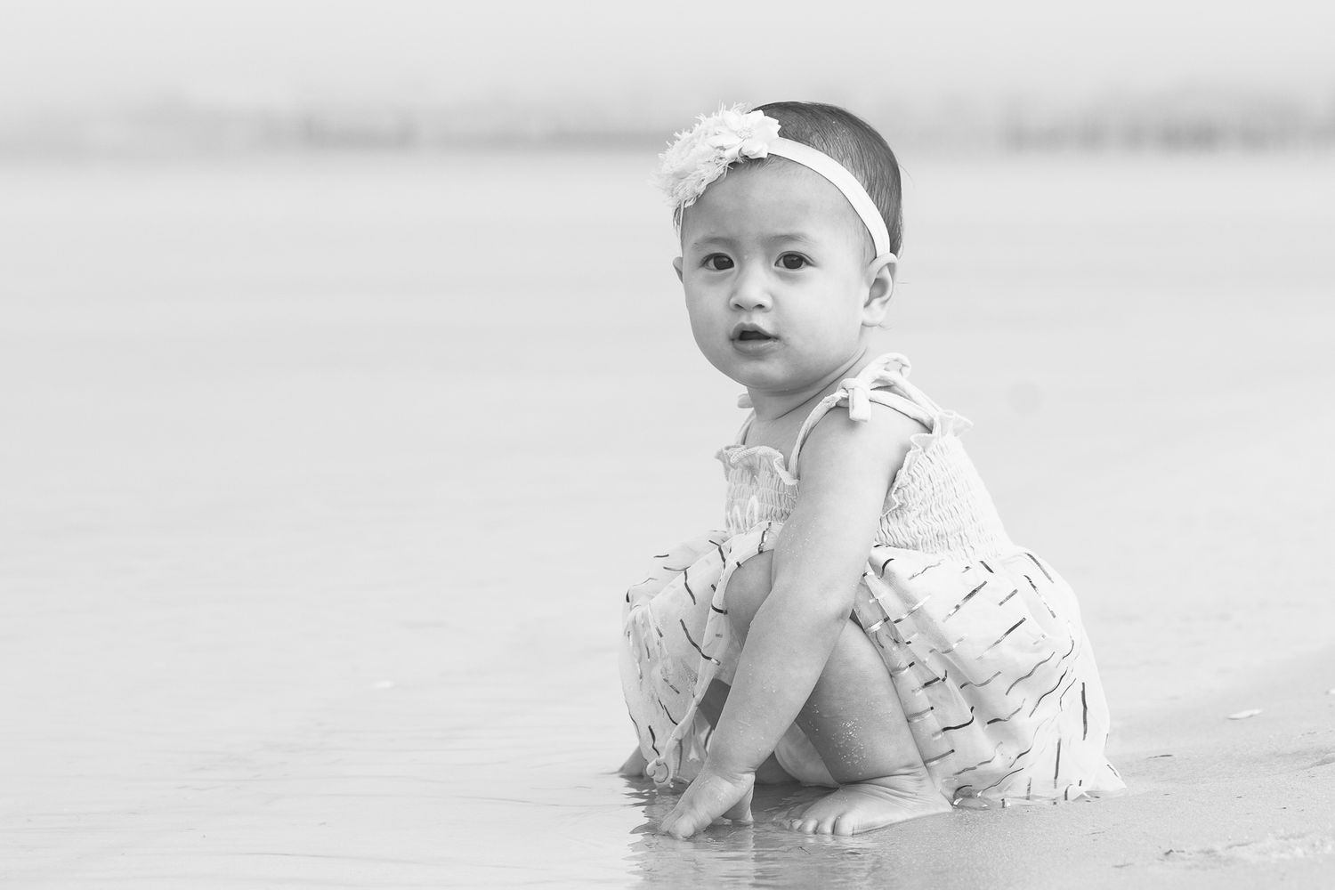Black and white photo of a baby girl sitting on the beach