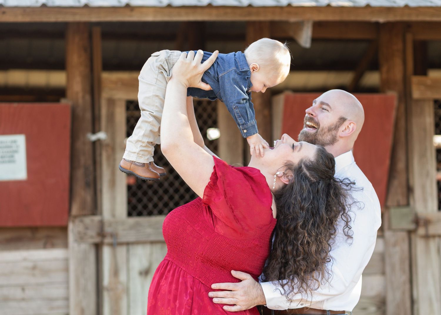 Mom lifting her baby into the air in front of a red barn