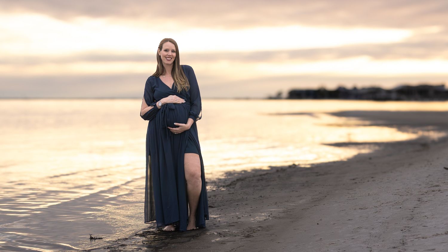 Pregnant woman standing on the shoreline at golden hour