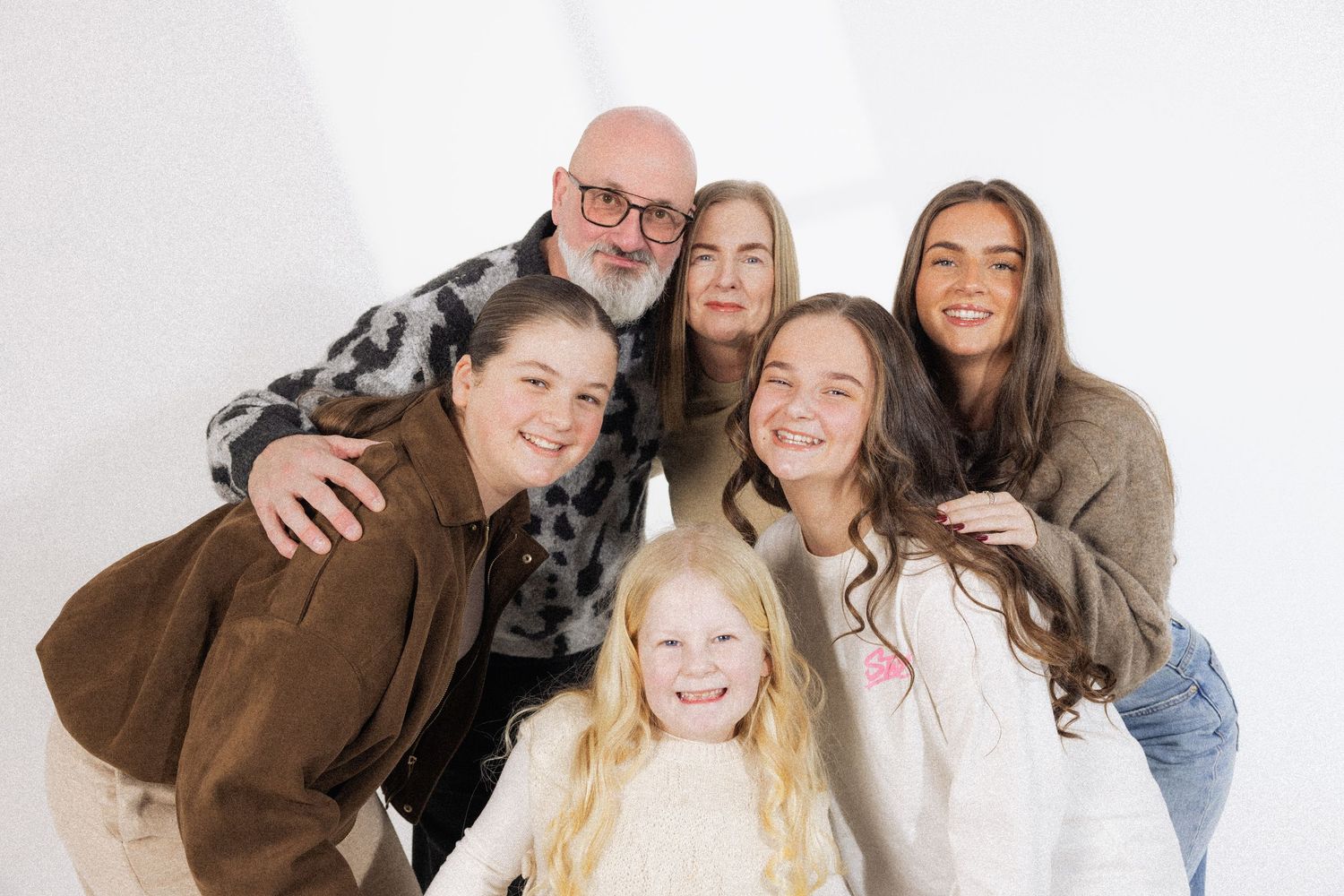Happy family of six poses together smiling against white background in casual portrait photo.
