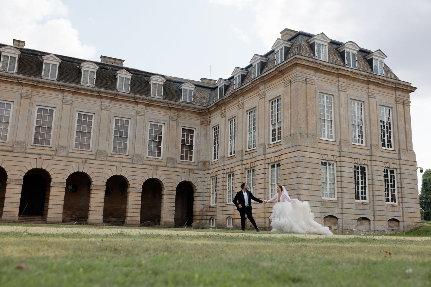 Bride and groom walk hand in hand across lawn before grand French chateau wedding venue.