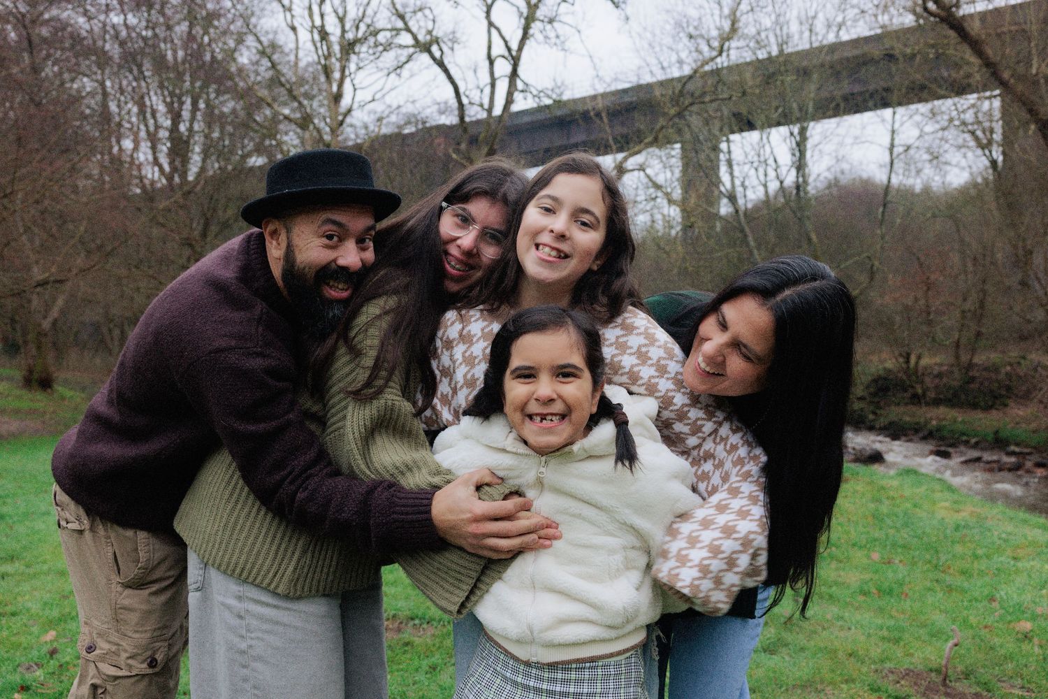 Joyful family of five sharing a warm group hug outdoors in a winter park setting.
