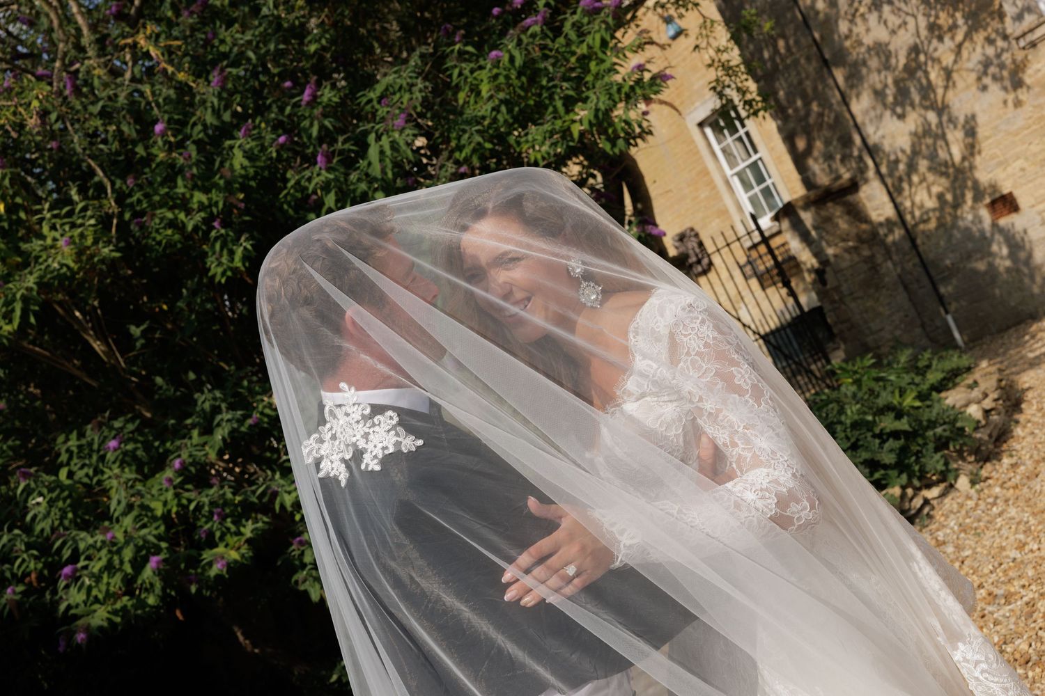 Bride wrapped in flowing white veil photographed from above in lush garden setting on wedding day.