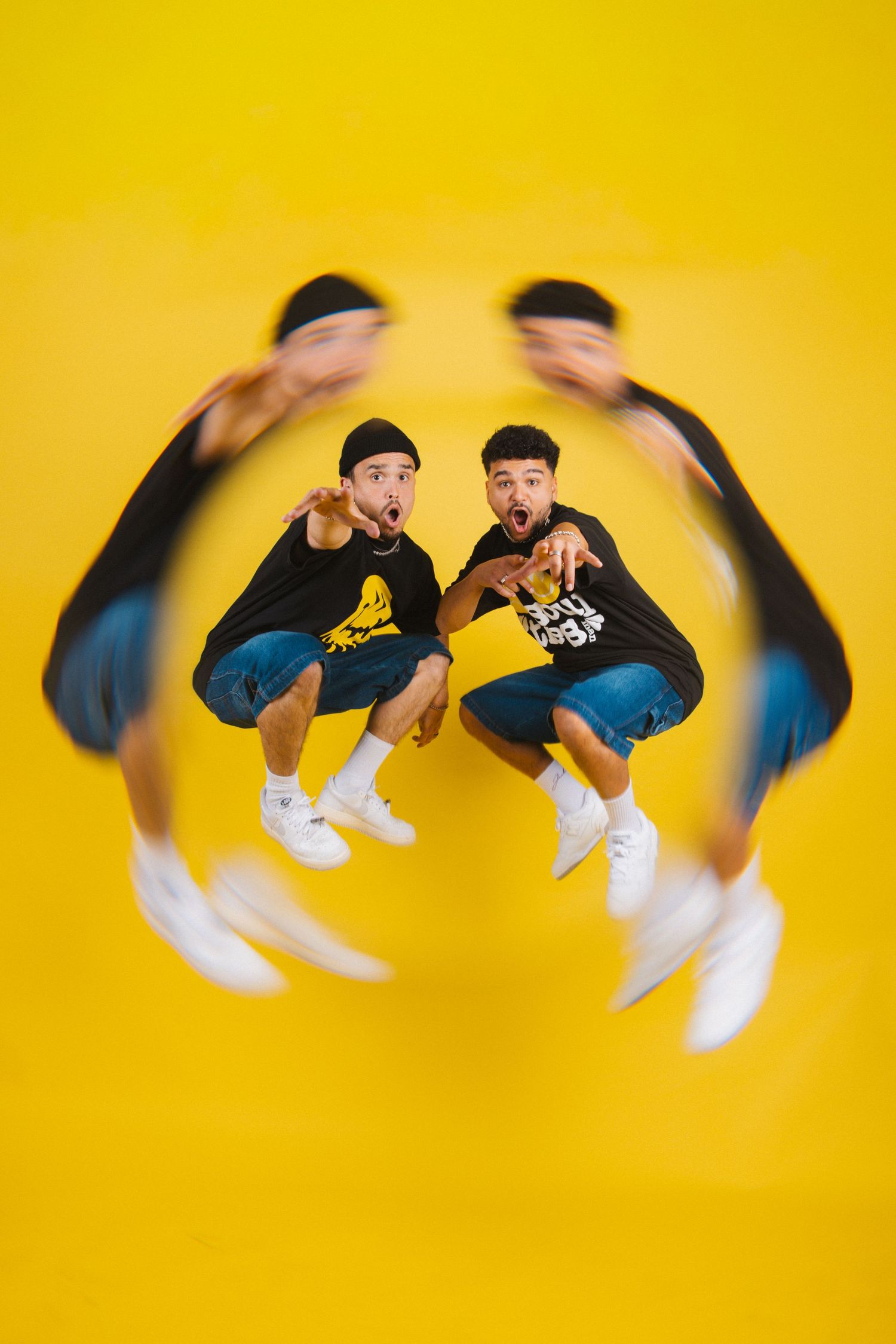 Two young men in black graphic tees crouching on yellow background with dynamic motion blur effect around them.