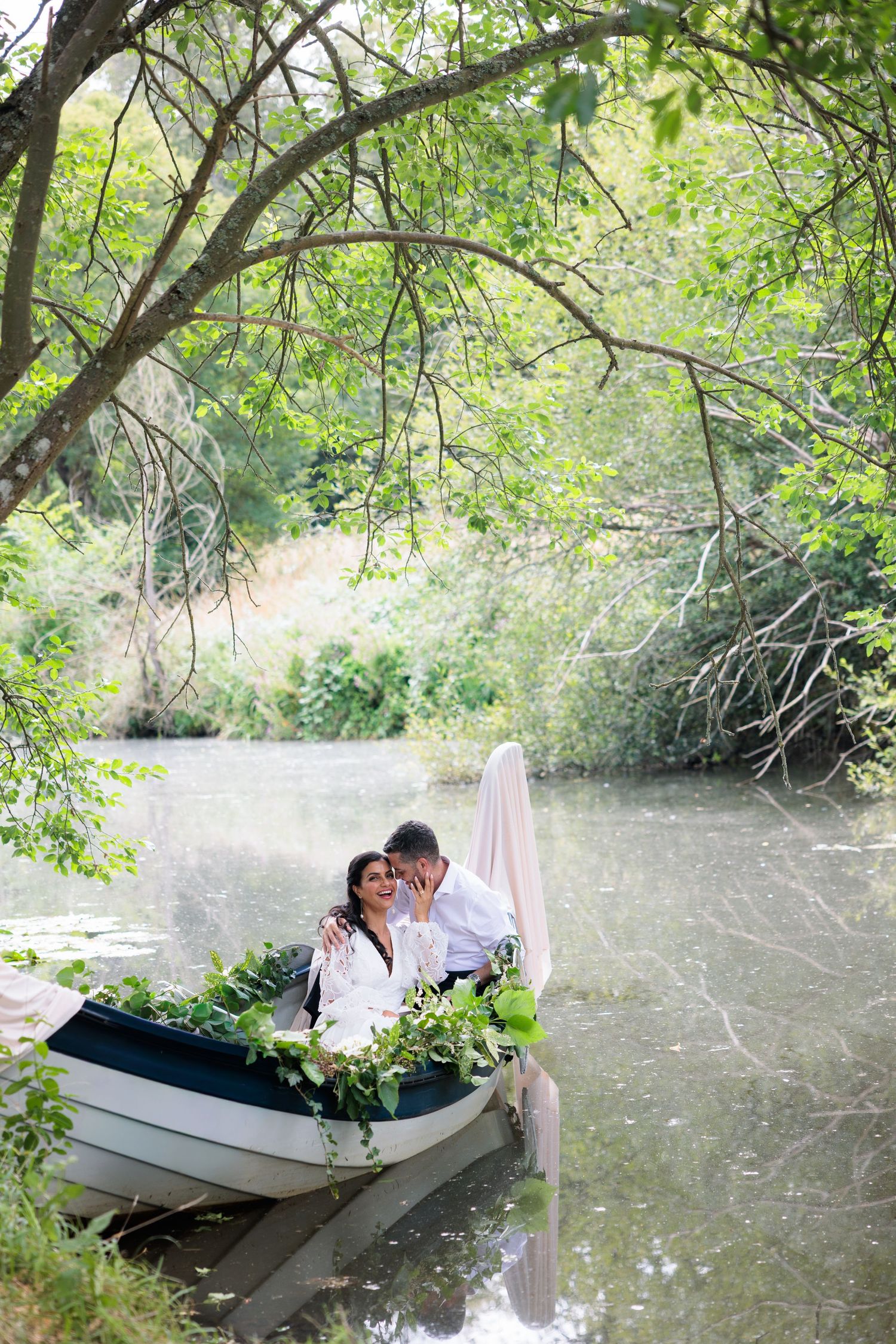 Romantic couple in white embrace in flower-decorated boat on tranquil tree-lined river. Greater Manchester