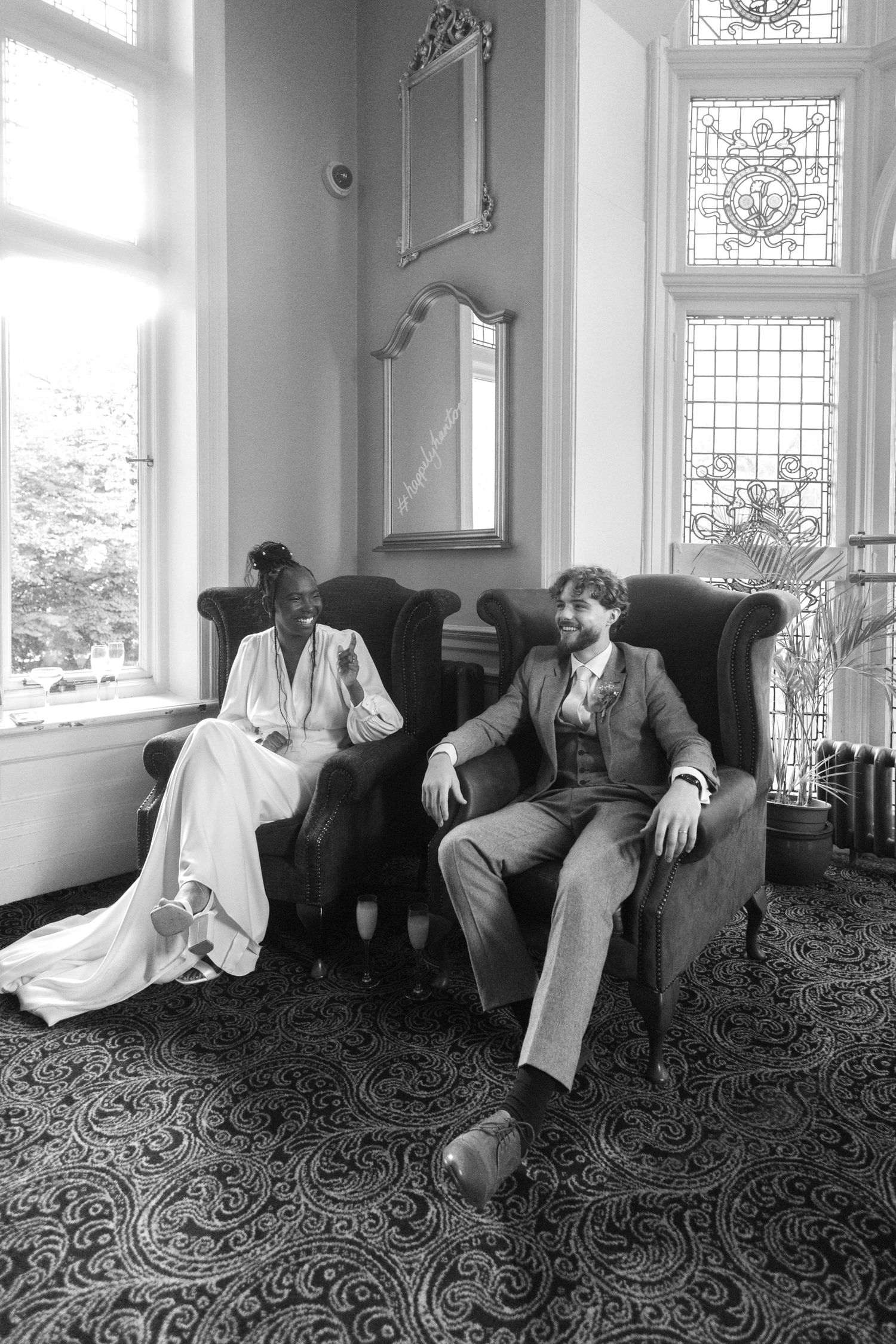 Black and white portrait of a bride and groom relaxing in armchairs in an elegant Victorian-style room. Didsbury Pub, Manchester Wedding