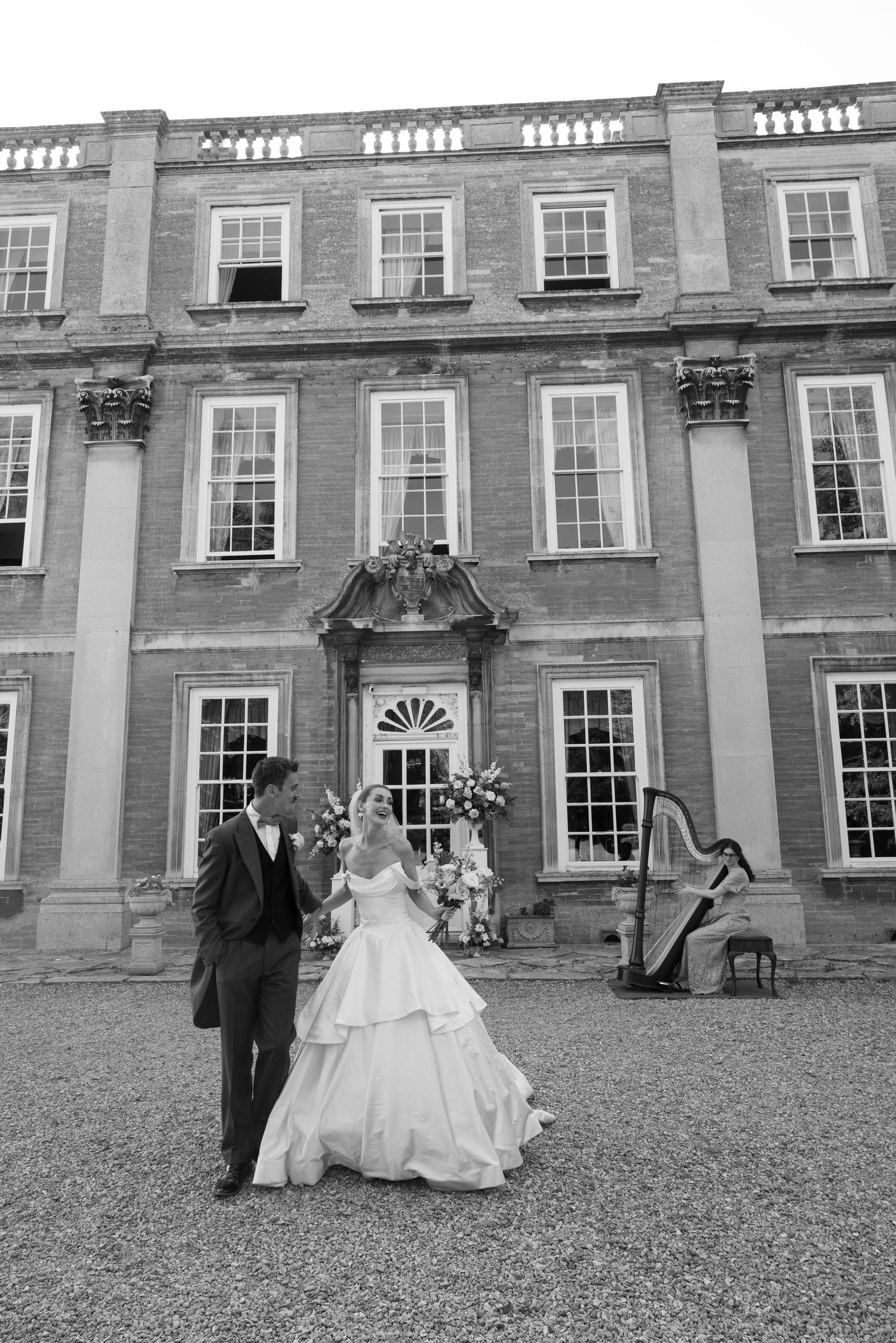 Black and white photo of bride and groom dancing outside elegant Georgian manor with harpist.