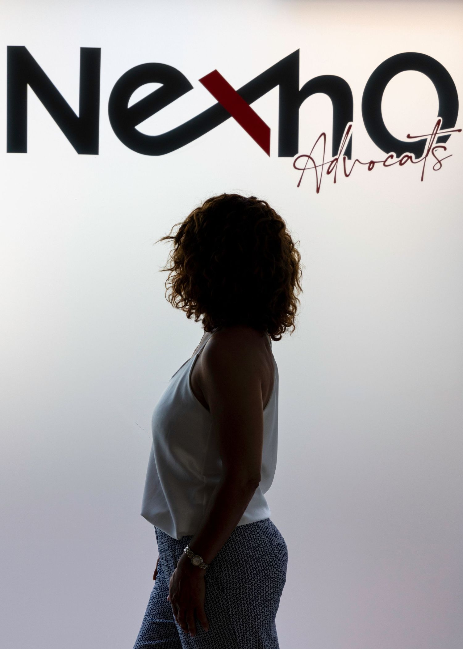 Silhouette of woman standing in front of illuminated Nexho Advocats logo. Lloret de Mar, Spain