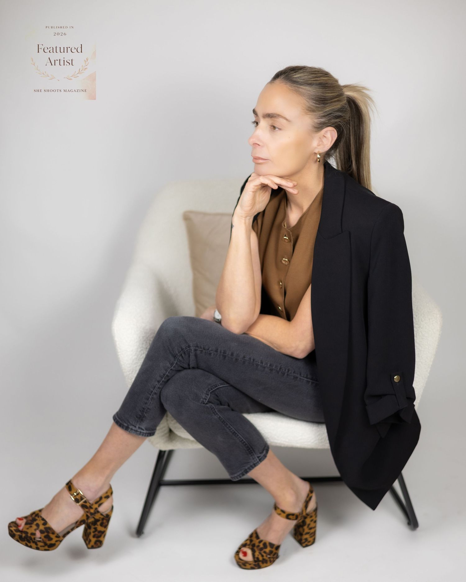 Stylish woman in black blazer and leopard heels sitting in white chair for featured artist portrait. South London Brand Photography