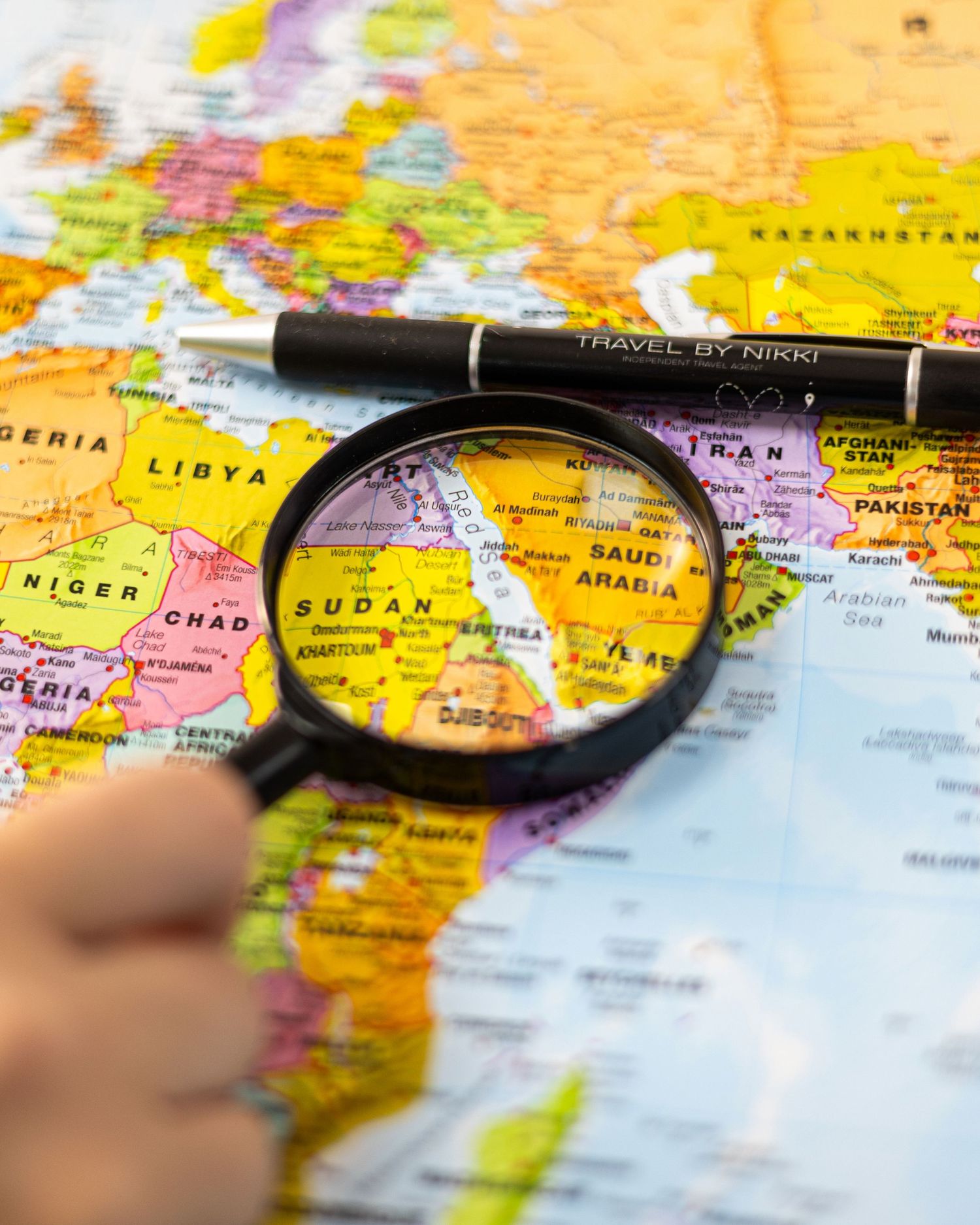 Hand holding magnifying glass over colorful world map focusing on Middle East and Africa region. South London Tavel Agent