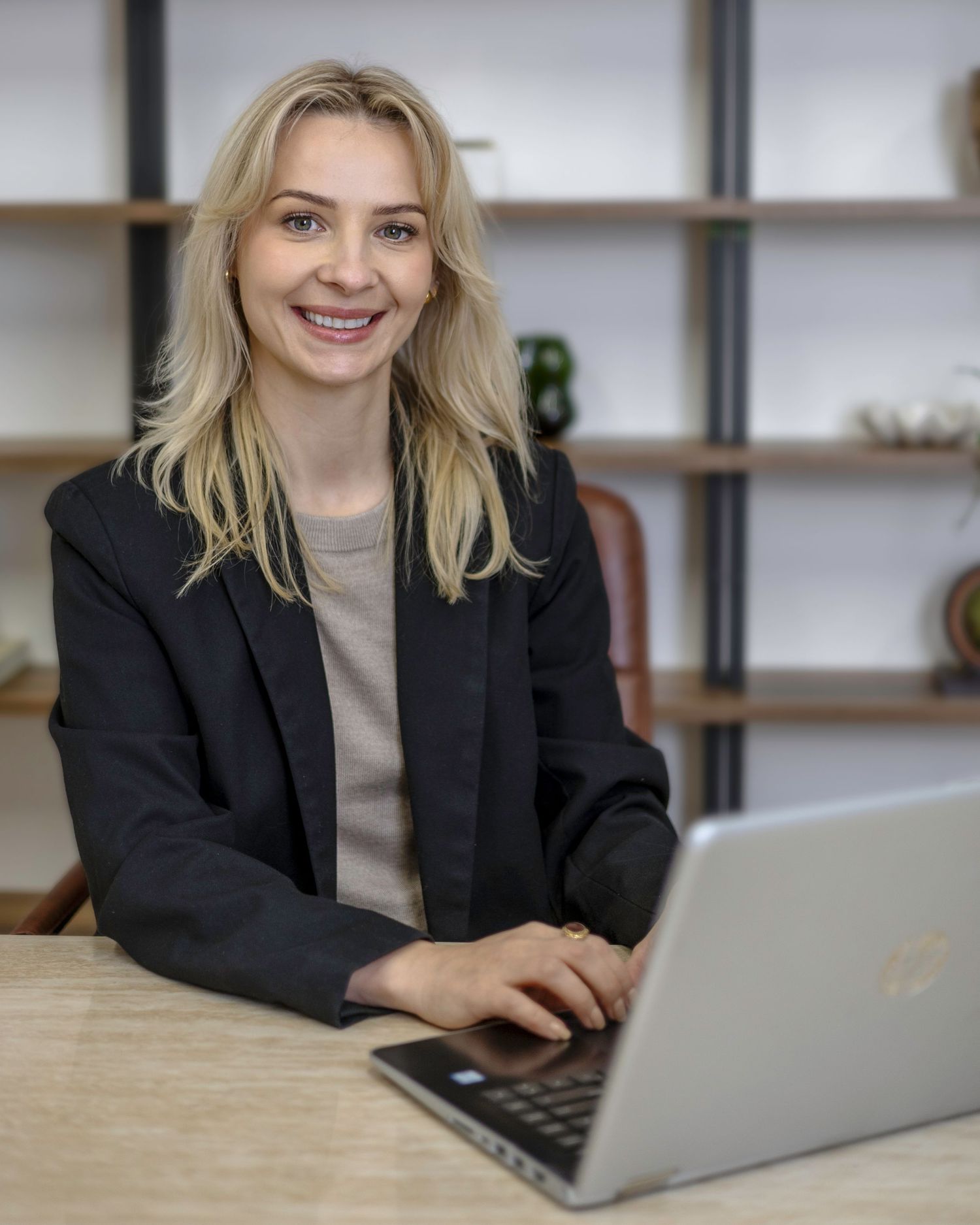 Smiling blonde woman in black blazer at desk with laptop. Moni Clayton Interiors, South London