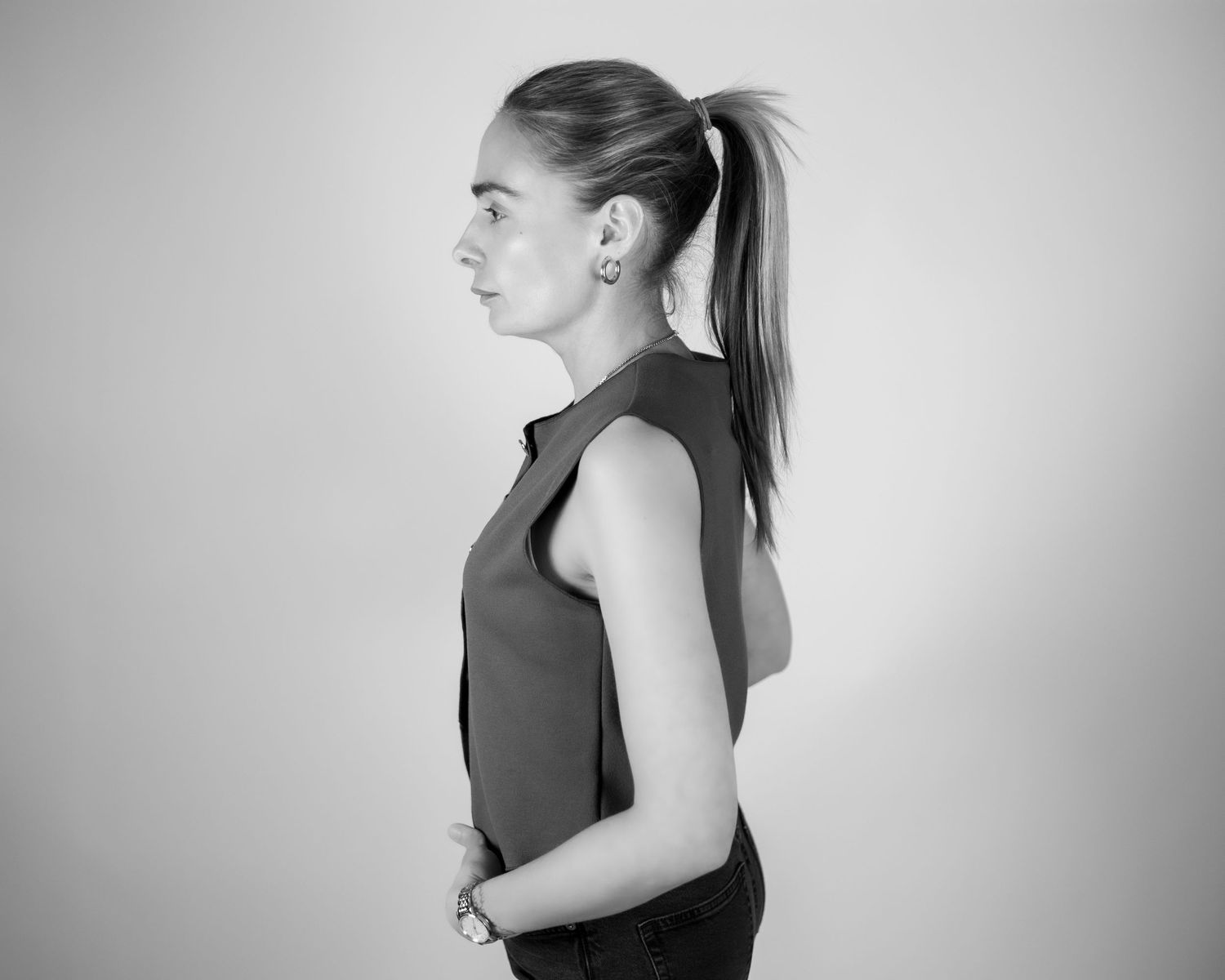 Side profile of young woman with ponytail wearing sleeveless top, black and white studio photo. Brand Photography South London