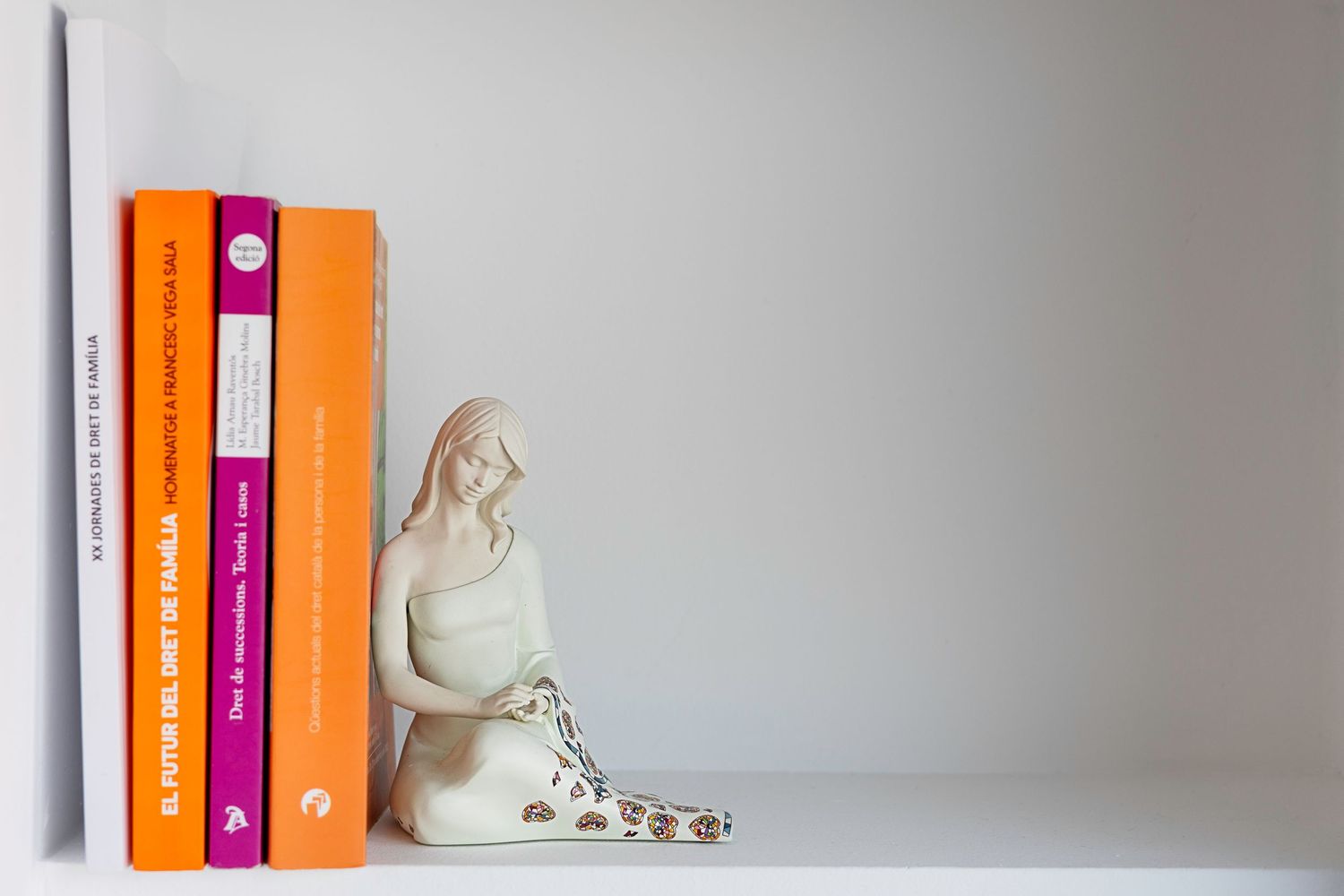 White ceramic Madonna figurine used as bookend beside colorful orange and yellow books on shelf. Lloret de Mar, Spain