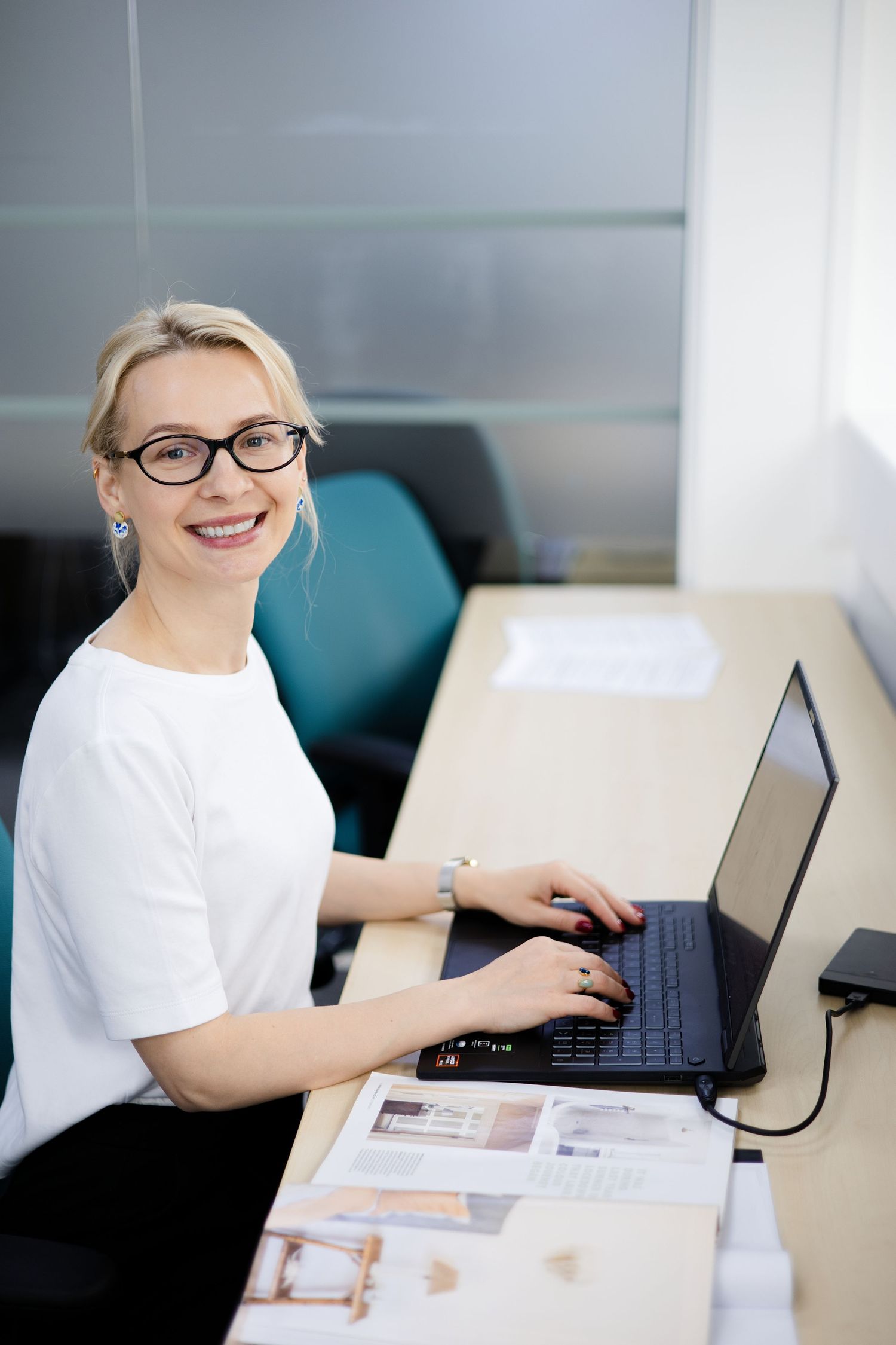 Smiling blonde businesswoman in glasses working on laptop at office desk with documents. Brand Photography South London