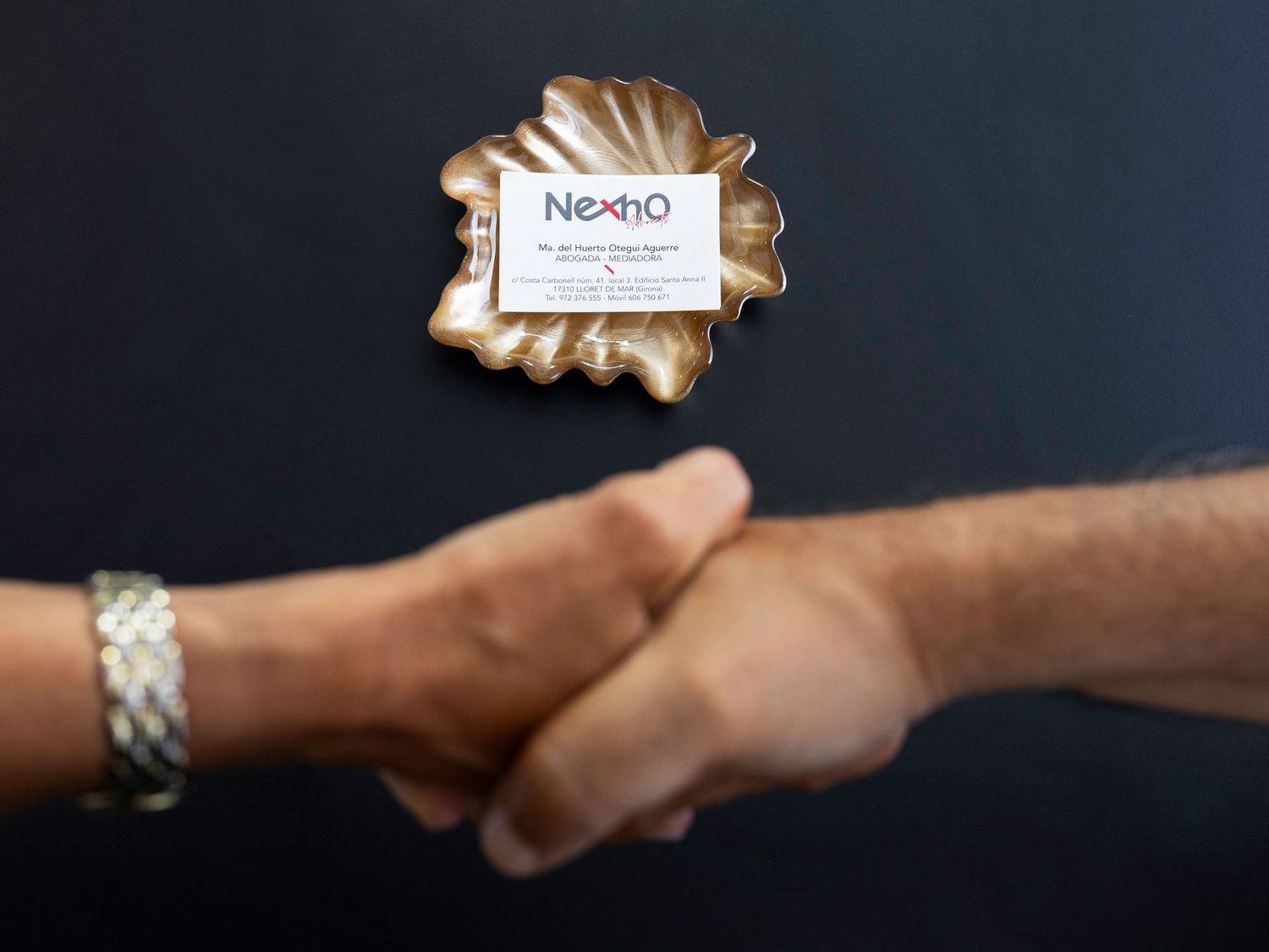 Two people shaking hands with Nexho business card on decorative dish. Lloret de Mar, Spain