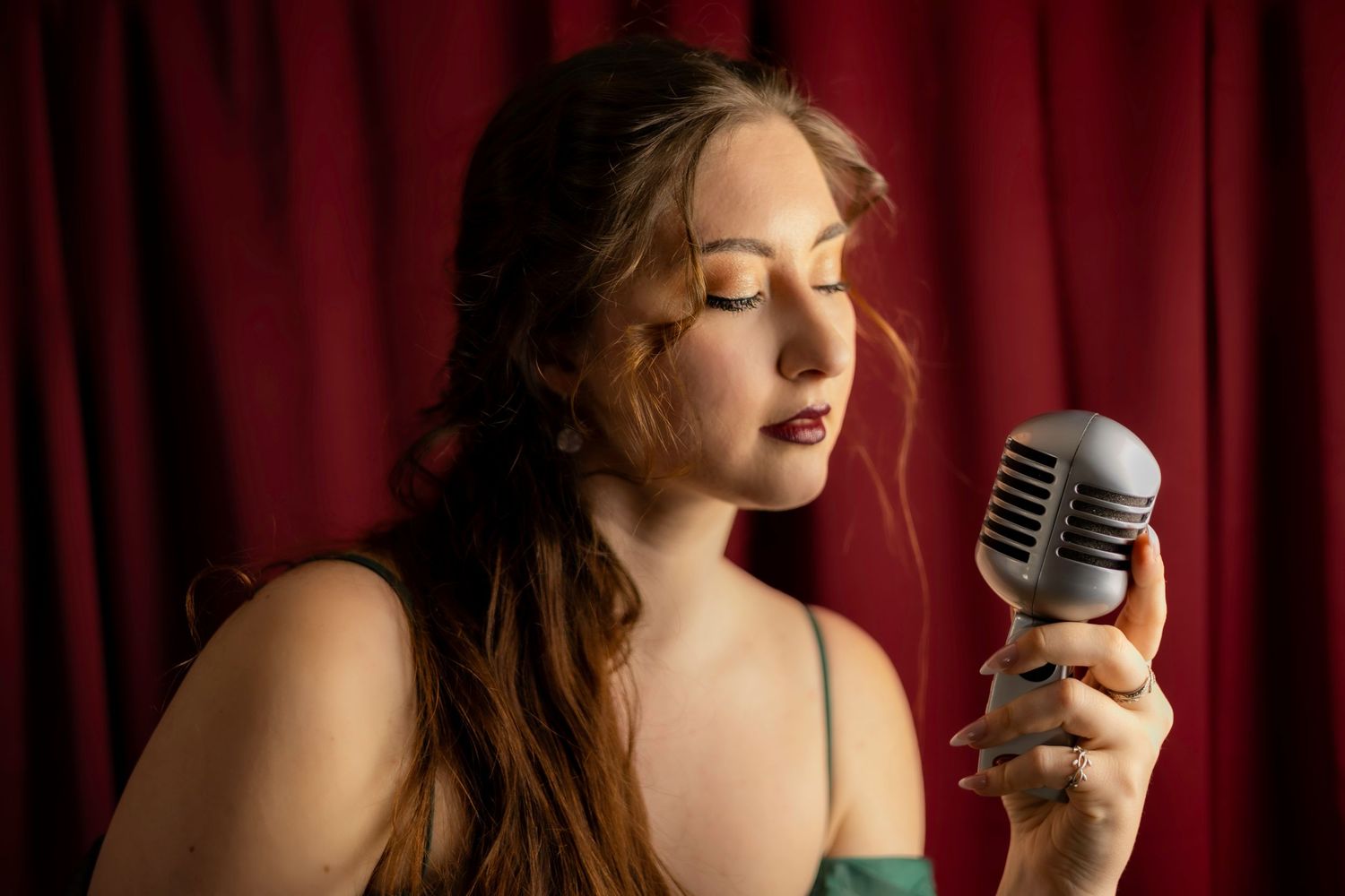 Young woman with long hair singing into vintage microphone against red curtain background. South London