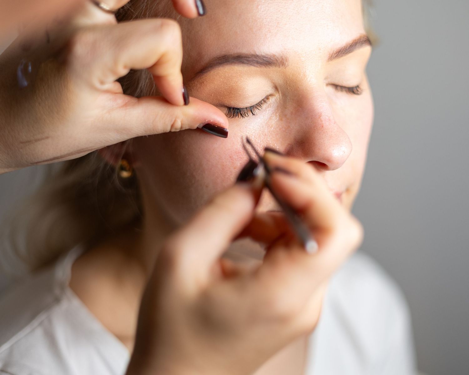 Makeup artist applying false eyelashes to a young blonde woman with closed eyes in a beauty salon. London